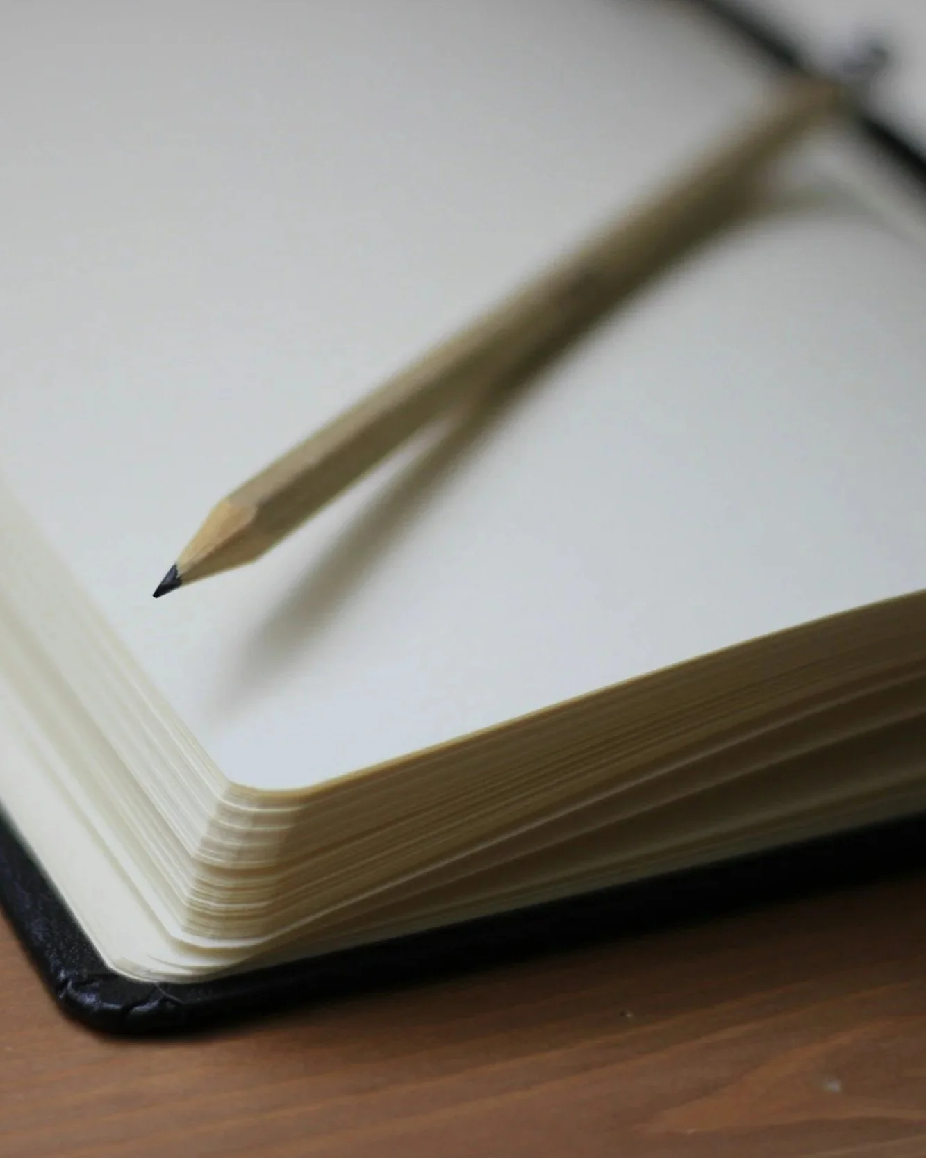 Close-up of a blank notebook with a sharpened pencil resting on top, placed on a wooden surface.