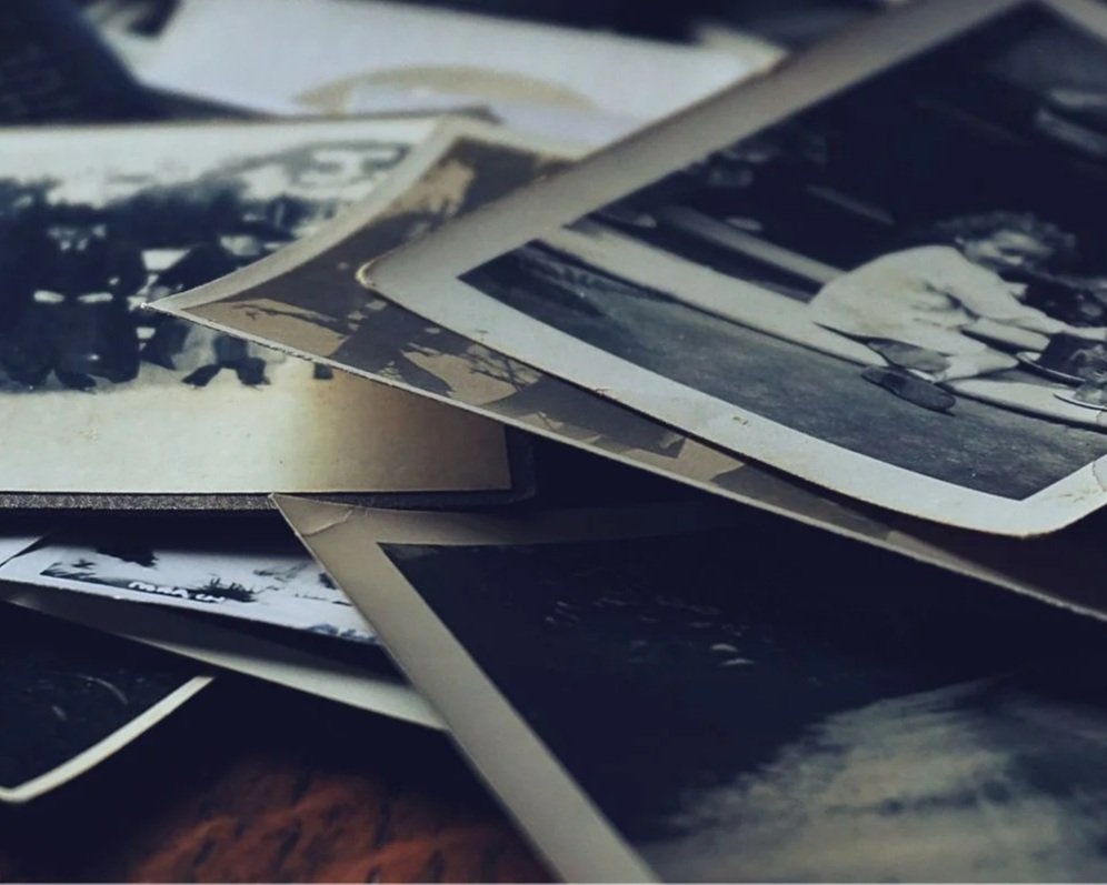 A collection of black-and-white printed photographs scattered and stacked on a surface.