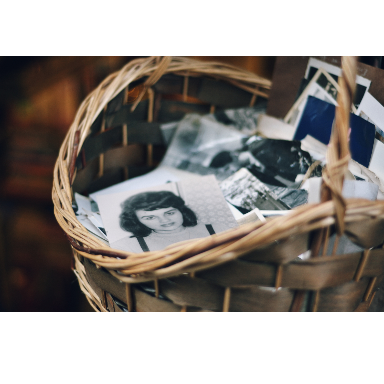 A collection of old black and white photographs arranged on a basket, evoking memories and reflection while choosing a photo for a memorial card.