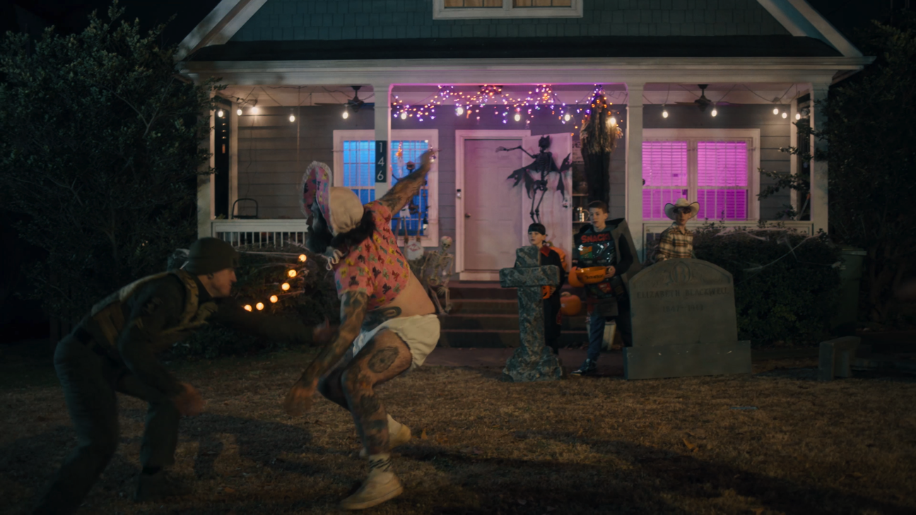 Children wearing costumes playing Halloween trick-or-treating outside a decorated house at night.