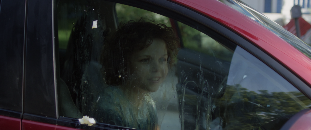 Child with curly hair looking out of a car window.