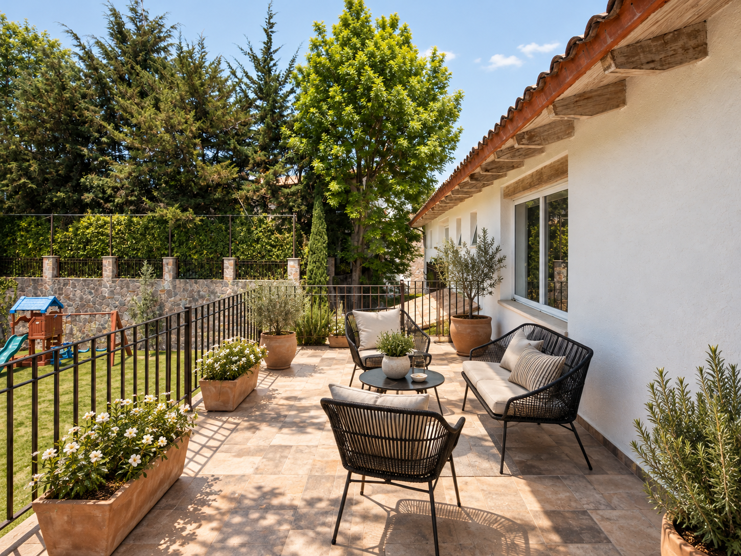 Terraza exterior de Rancho San Bartolo con sillones de mimbre, macetas y barandal hacia el jardín.
