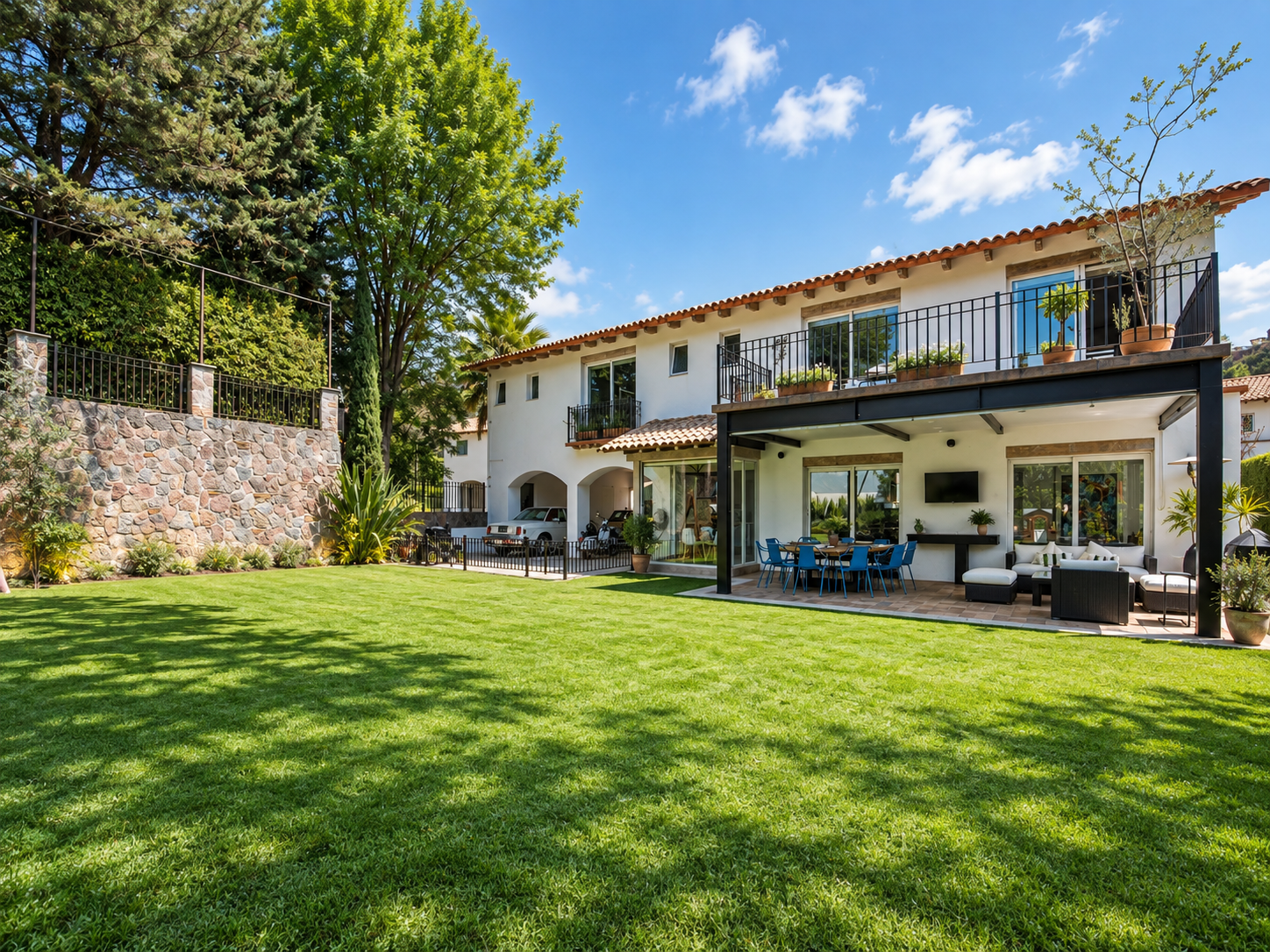 Jardín de Rancho San Bartolo con césped amplio, árboles y fachada de dos niveles junto a la cochera.