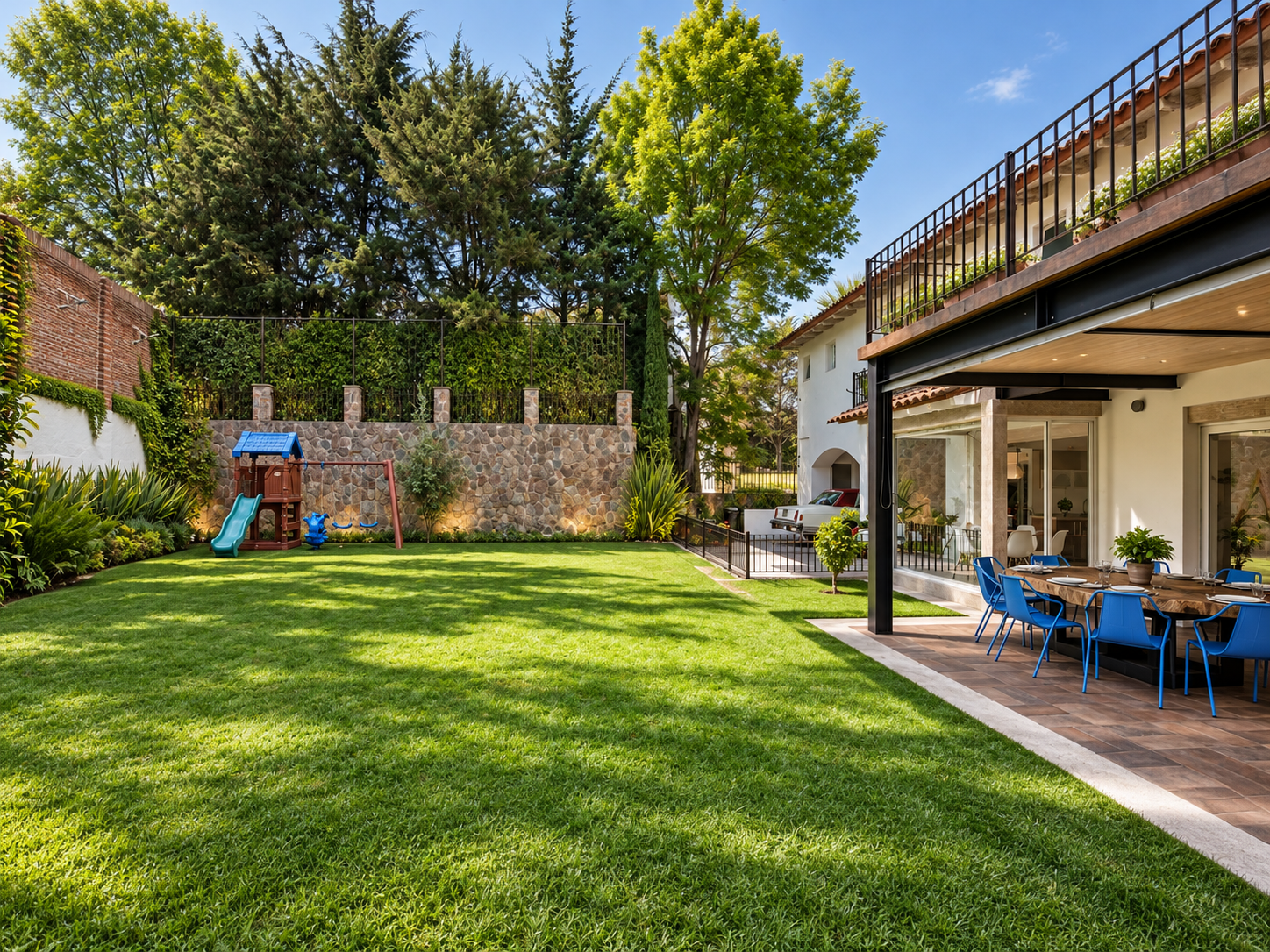 Vista del jardín de Rancho San Bartolo hacia la casa, con césped, terraza y árboles.