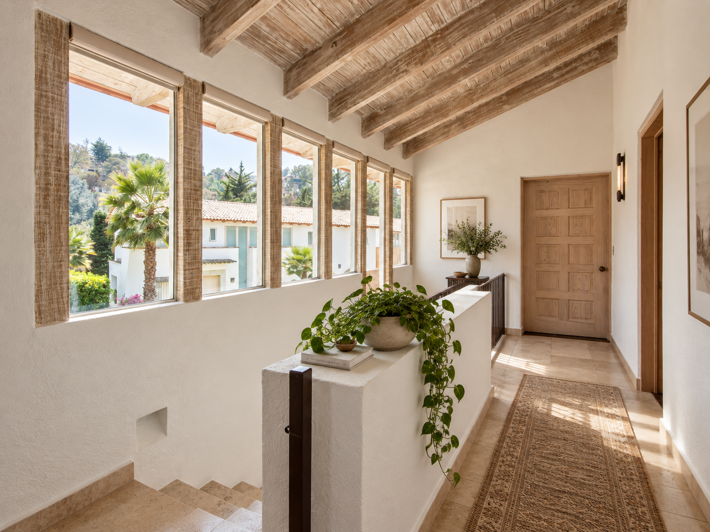 Pasillo de planta alta de Rancho San Bartolo con ventanales hacia los árboles, vigas de madera y barandal junto a la escalera.