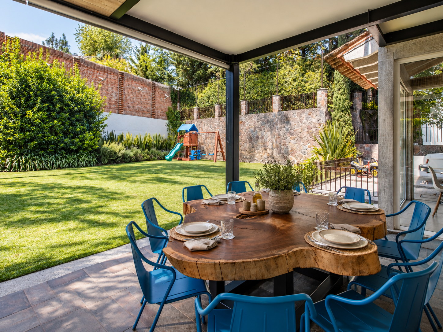 Comedor de terraza de Rancho San Bartolo con mesa redonda de madera, sillas azules y vista al jardín.