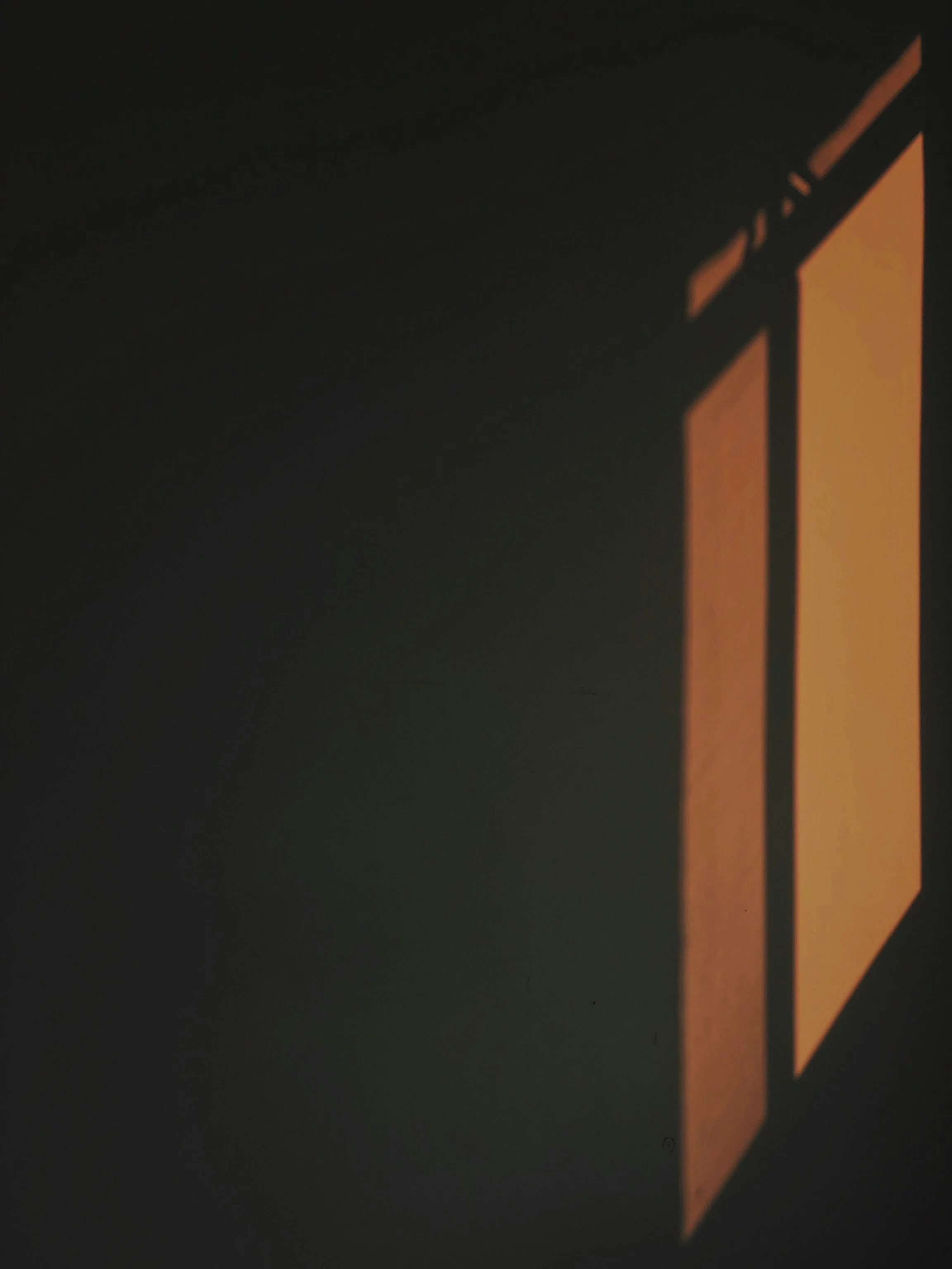 A shadow of a rectangular object projected on a wall, with its shape resembling a window or poster with orange and black colors.