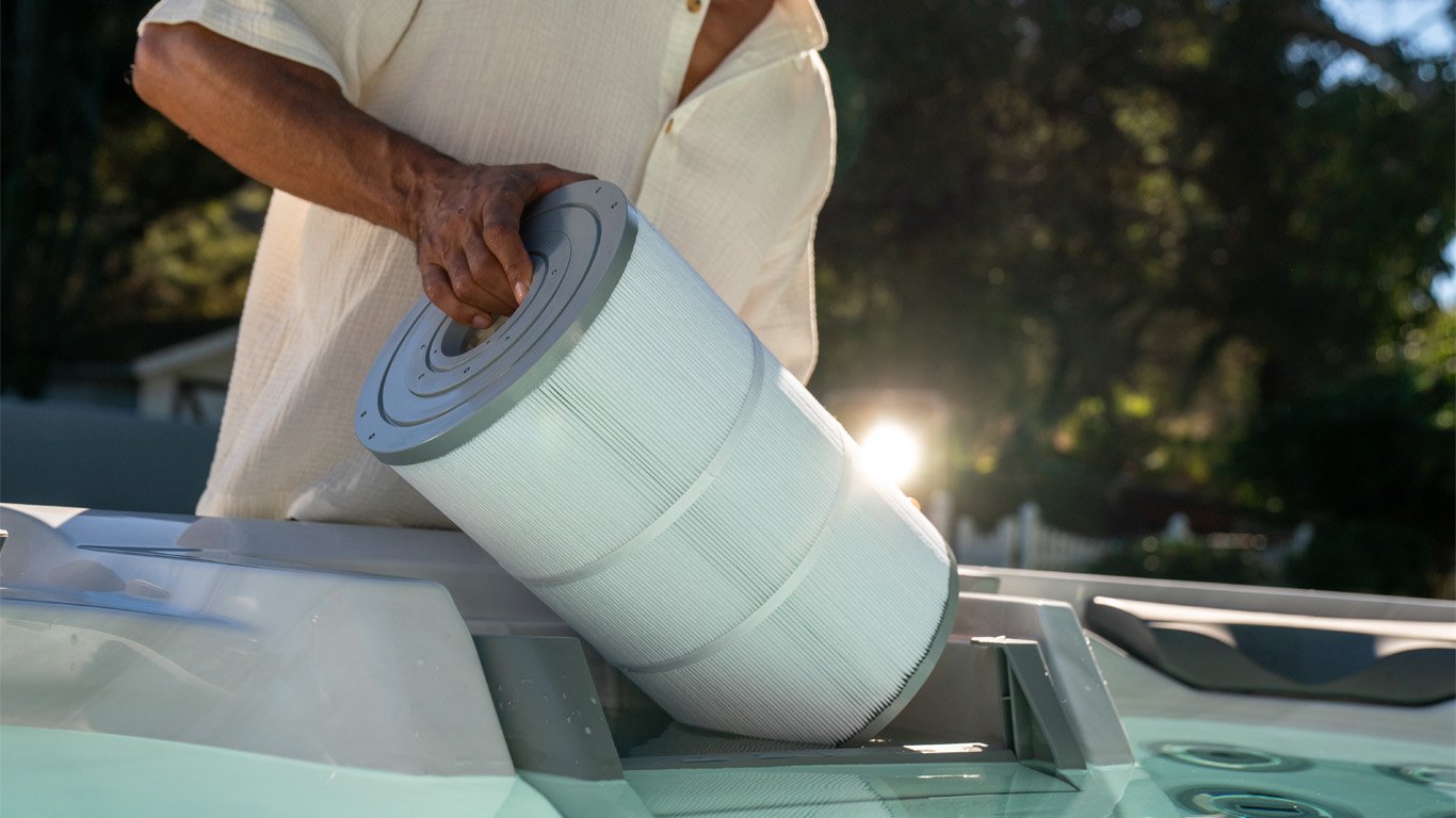 A person removes a MicroClean® Ultra II Filtration cylindrical filter cartridge from a hot tub under sunlight.