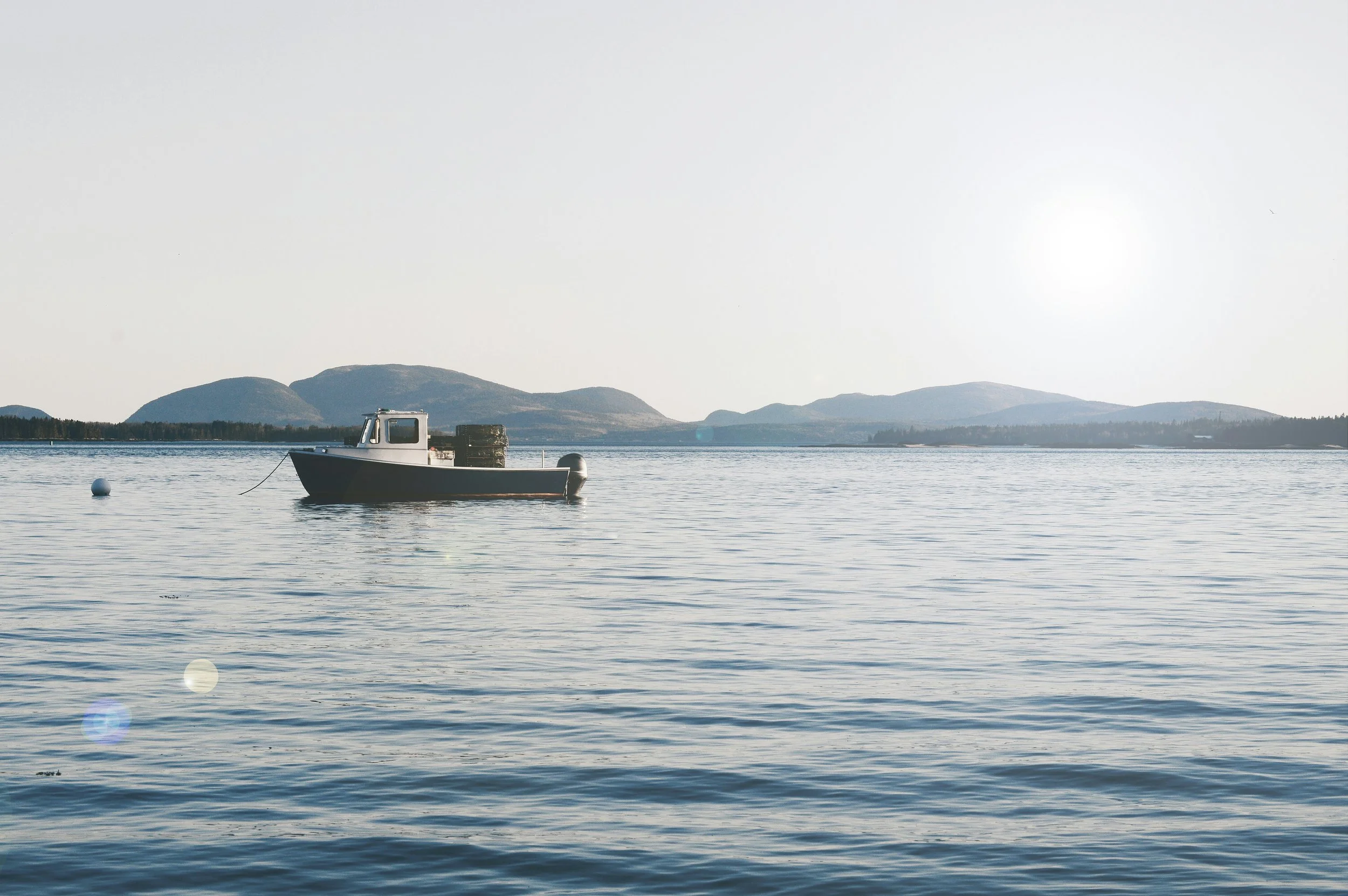 A boat floating on calm water with distant mountains and a bright sky in the background.