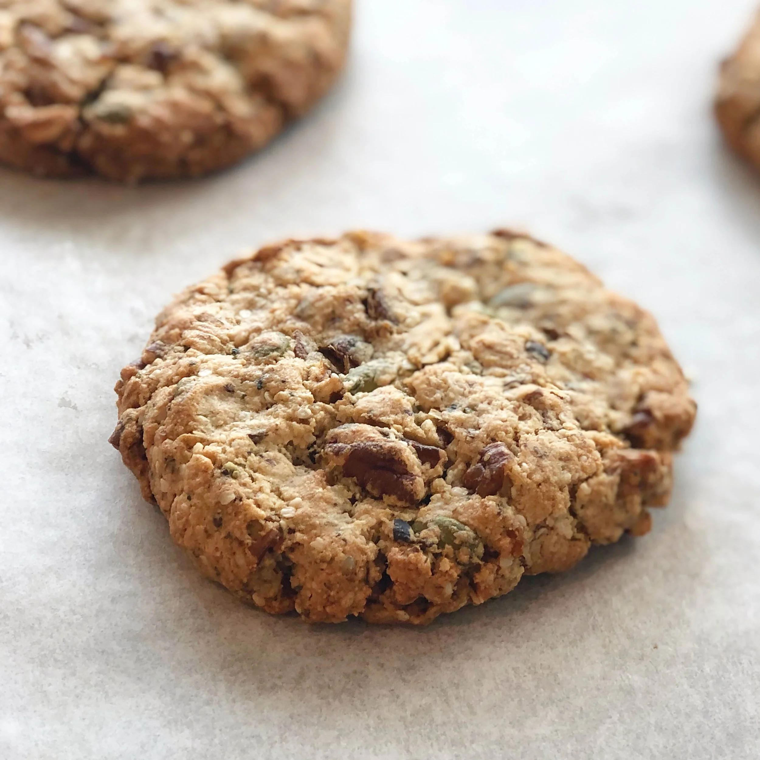 Close-up of a homemade oatmeal cookie with visible oats and chocolate chips on a white surface.