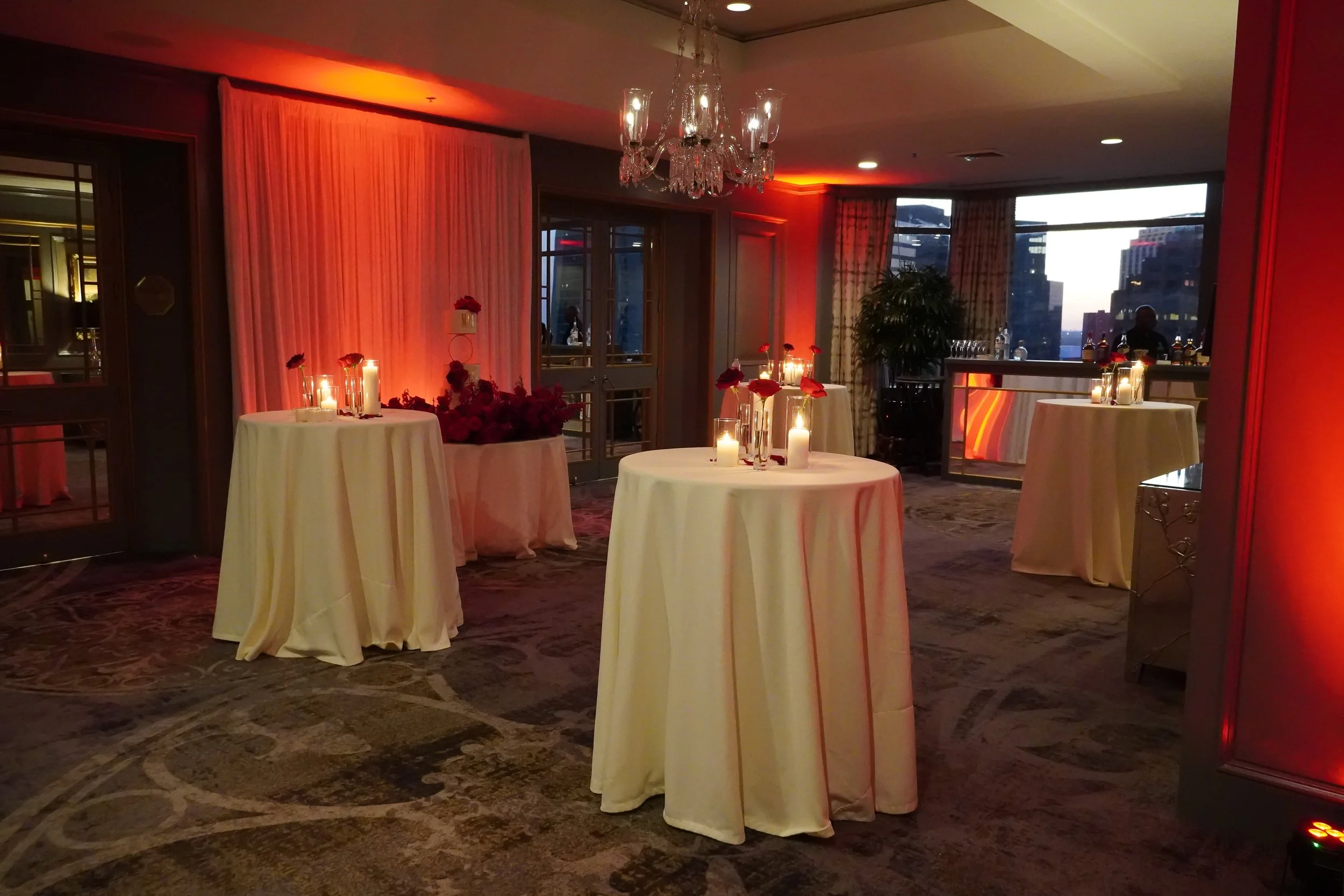 Elegant New Orleans event space with candlelit tables, floral arrangements, chandeliers and warm reception lighting.
