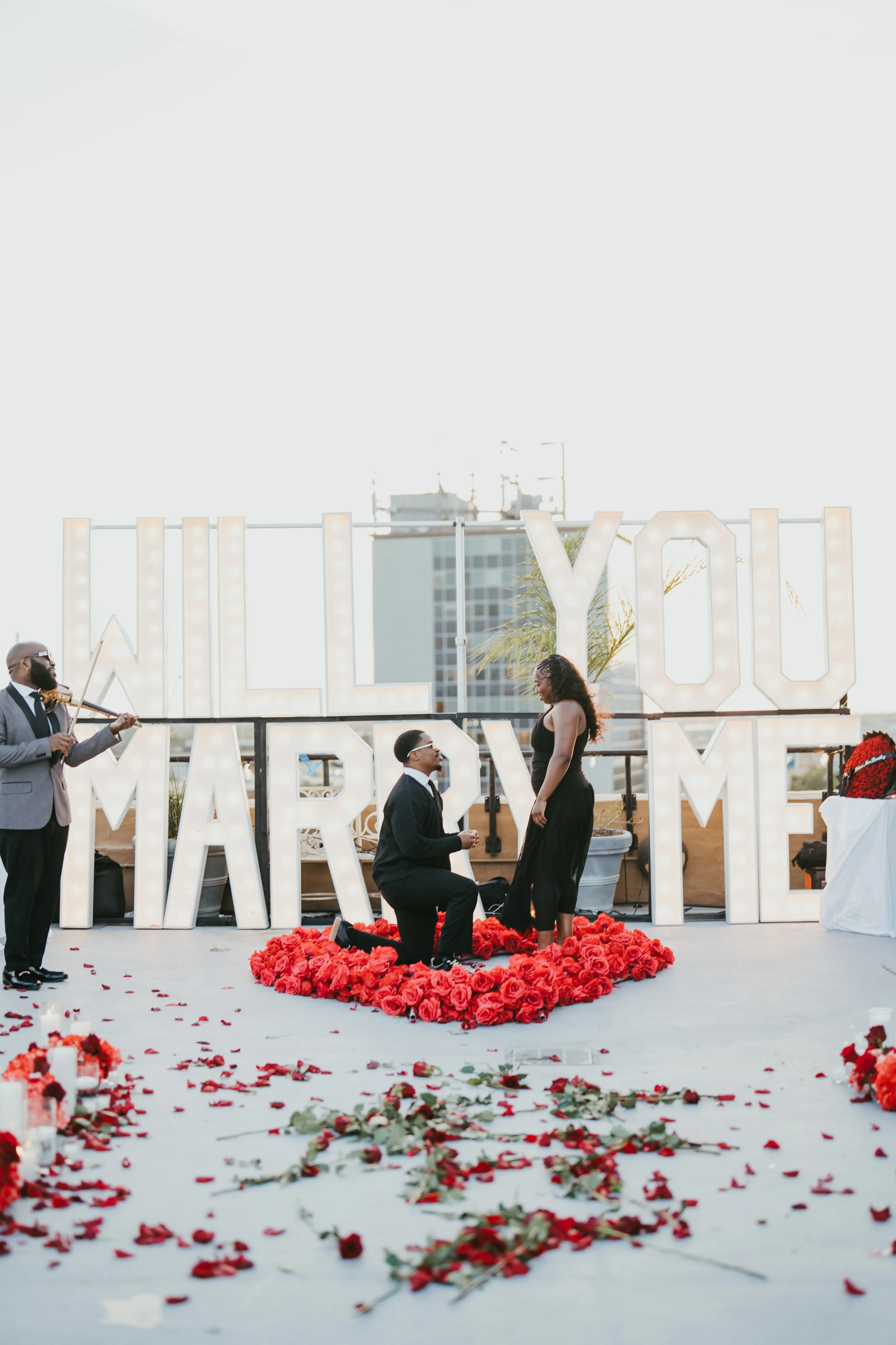 Rooftop marriage proposal in New Orleans with a red rose heart, rose petals and Marry Me Marquee letters.