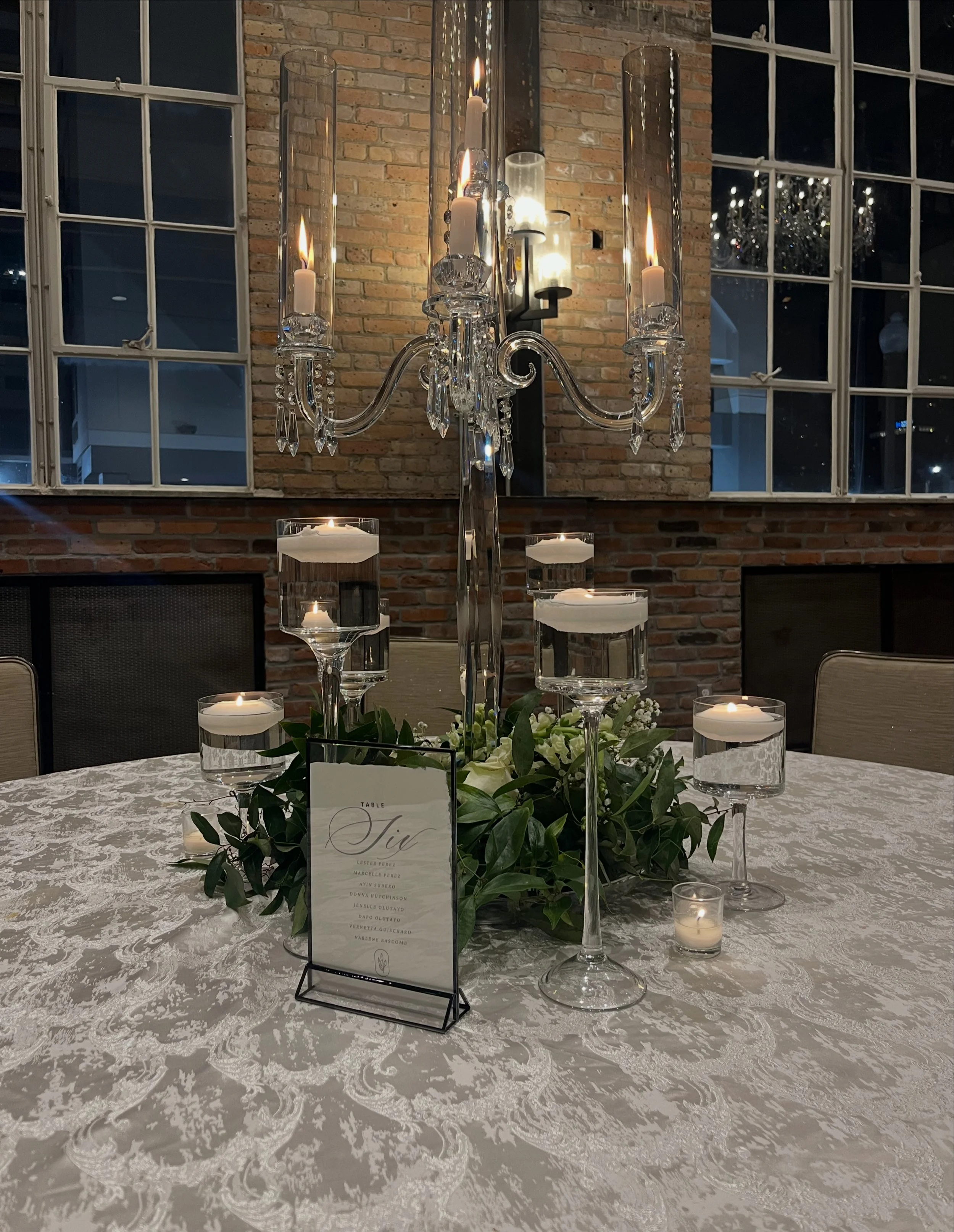 Elegant wedding table scape featuring white floral, greenery and floating candles in glass cylinders.