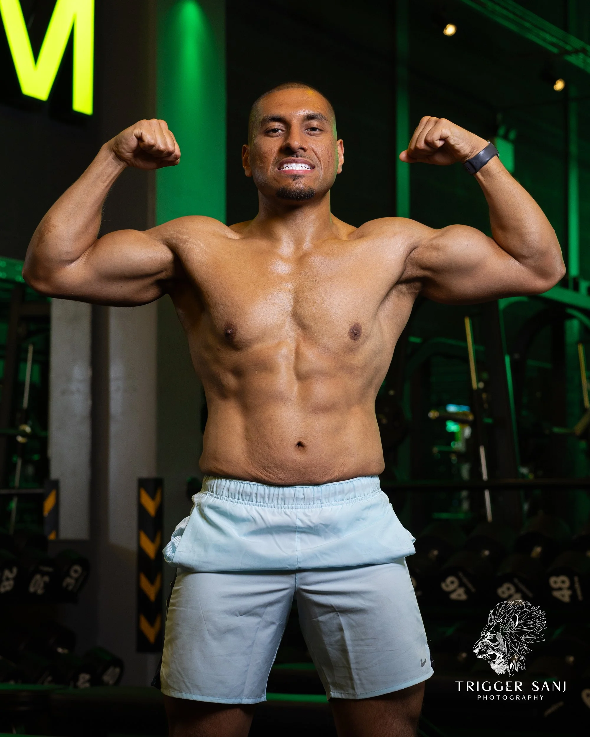 Portrait photo of a male fitness trainer flexing abs and biceps in Energym West Ealing