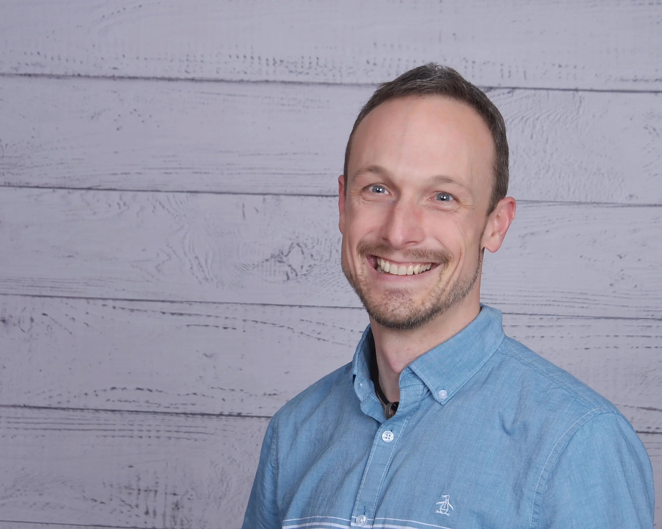 trey chatain author headshot wearing blue button down shirt against wood wall