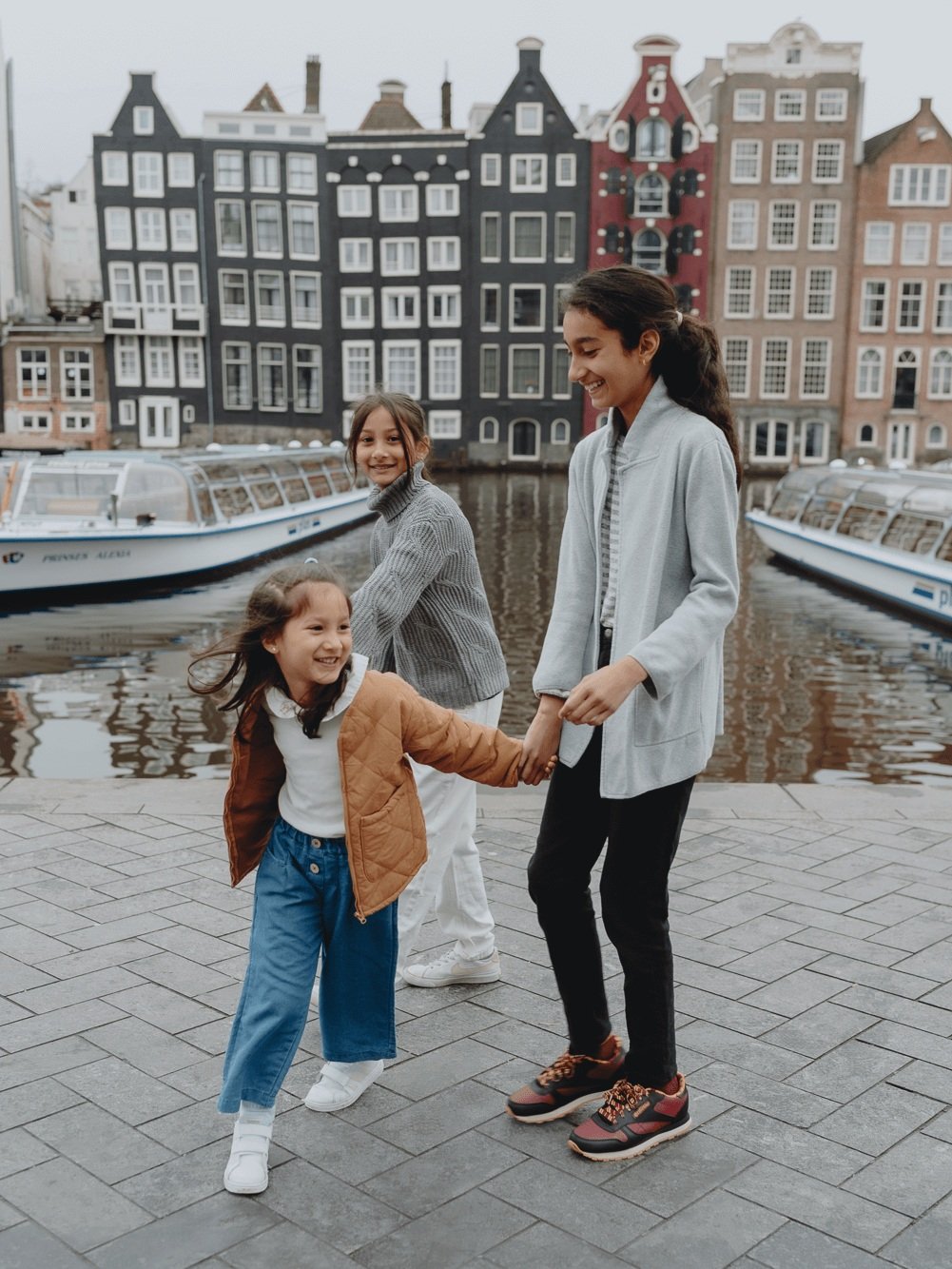 Family Photoshoot in Amsterdam by Vicky McLachlan Photography - American Family with three sisters standing together in front of Damrak in Amsterdam with Dutch buildings and boats in the background_1-1.png