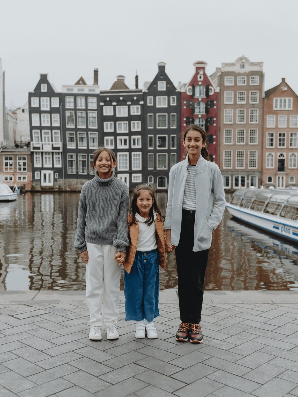 Family Photoshoot in Amsterdam by Vicky McLachlan Photography - American Family with three sisters standing together in front of Damrak in Amsterdam with Dutch buildings and boats in the background-1.png