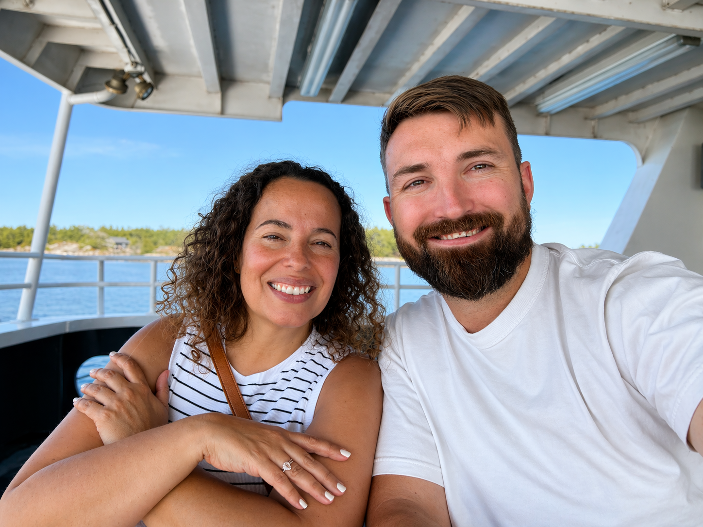 A smiling woman and man taking a selfie on a boat with blue water and a small island in the background.