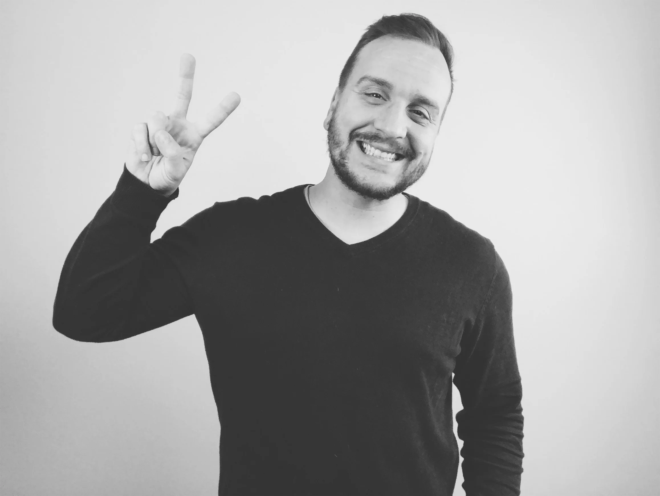  Image Description: a black and white studio photo of Matt smiling and gesturing the peace sign. 