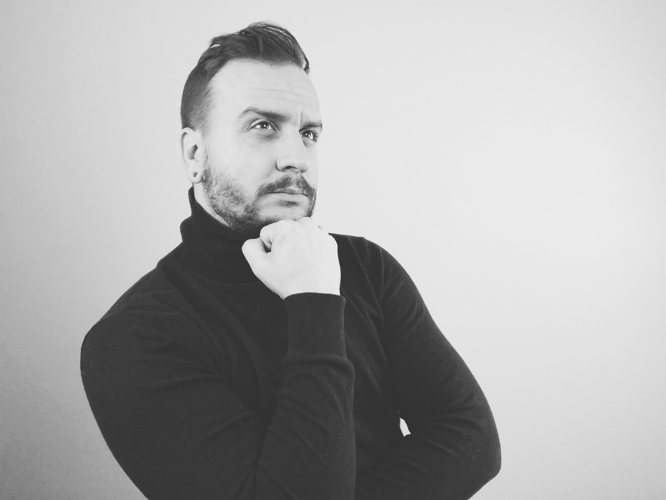  a black and white studio photo of Matt thinking with his head resting on a fist. 