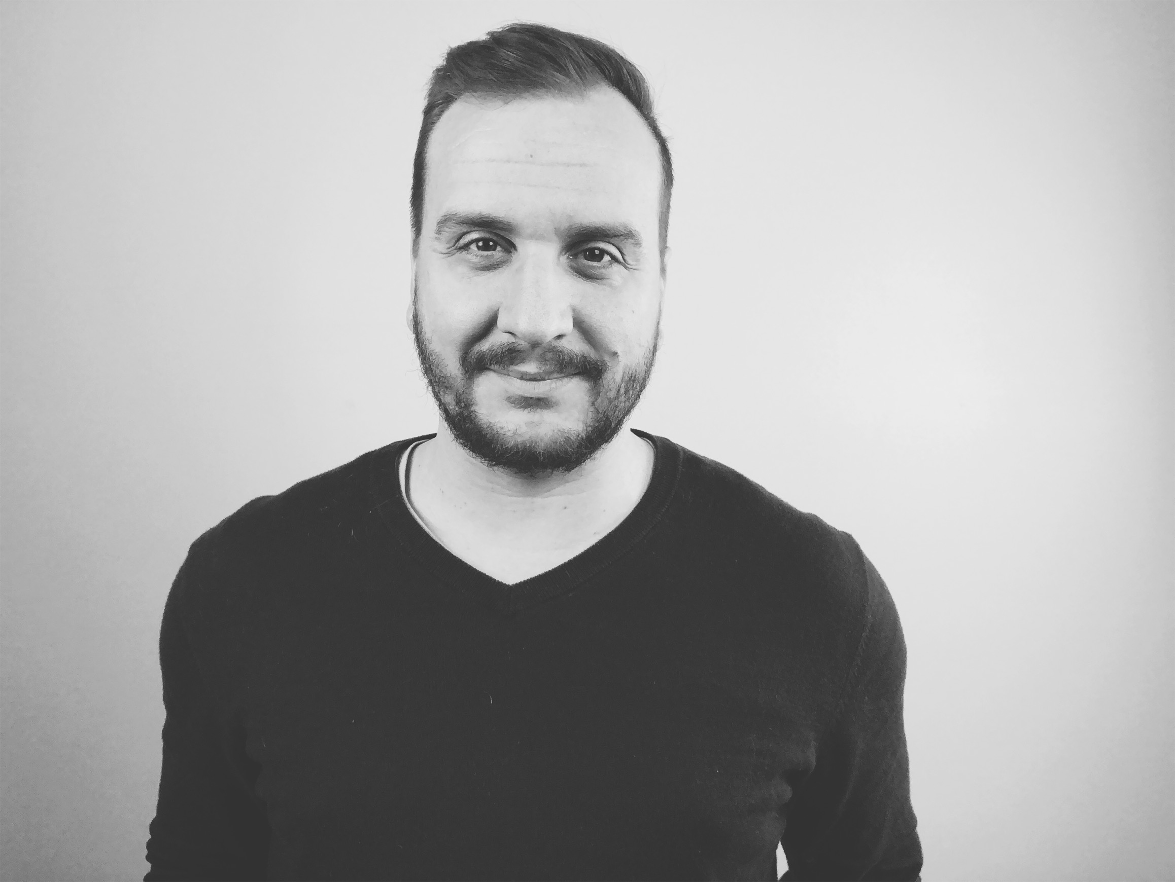 Image Description:  A black and white photo of Matt smirking and wearing a black v-neck sweater.