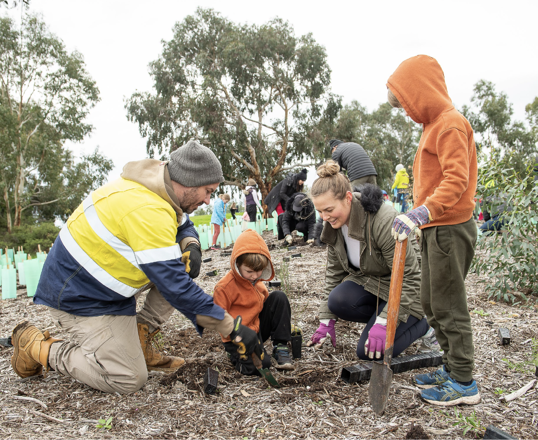 A man, a woman and two children are outside planting together as part of a community planting day