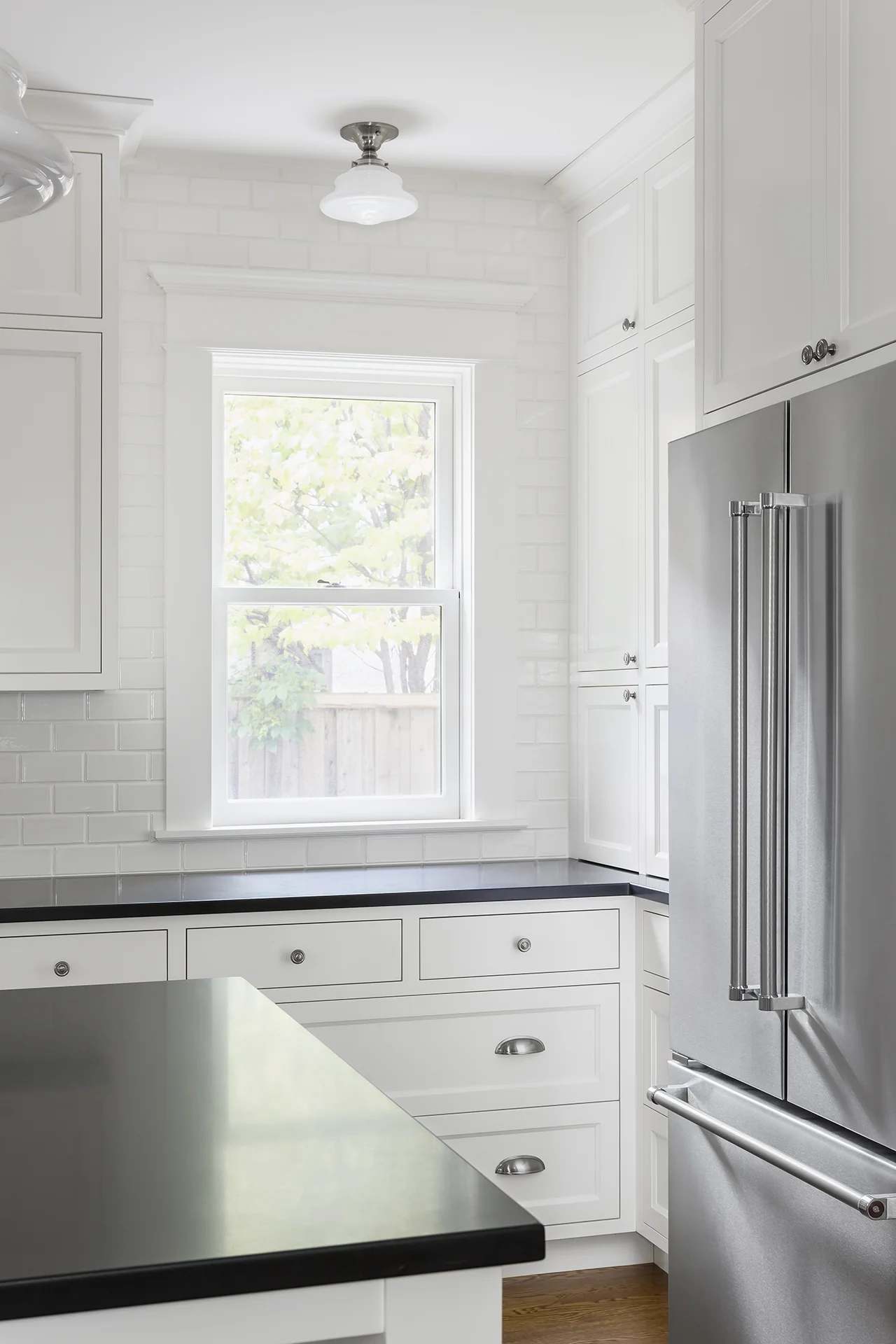 Classic inset doors and drawers, satin nickel hardware and reproduction lighting are nods to the past, while stainless steel appliances, honed-granite countertops and a center island add modern touches.