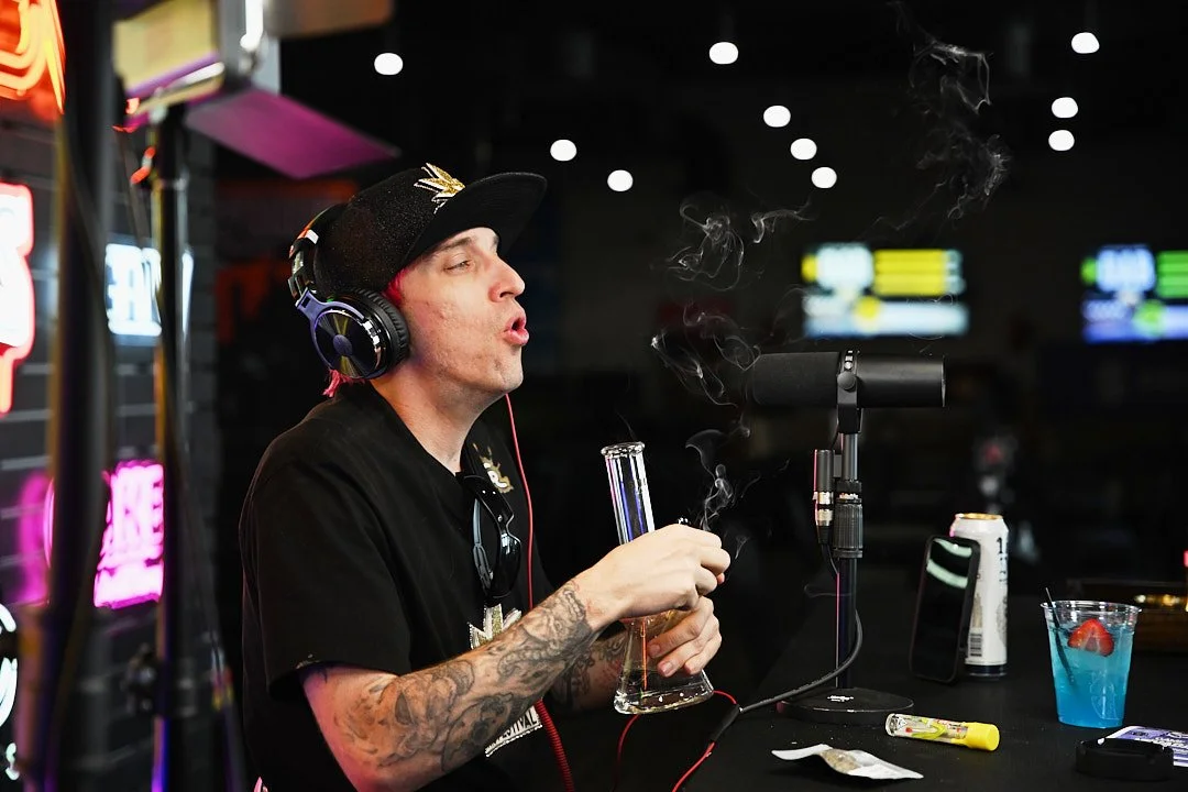 Sheldon speaks into a podcast microphone while using a glass water pipe inside Sky High Lounge.
