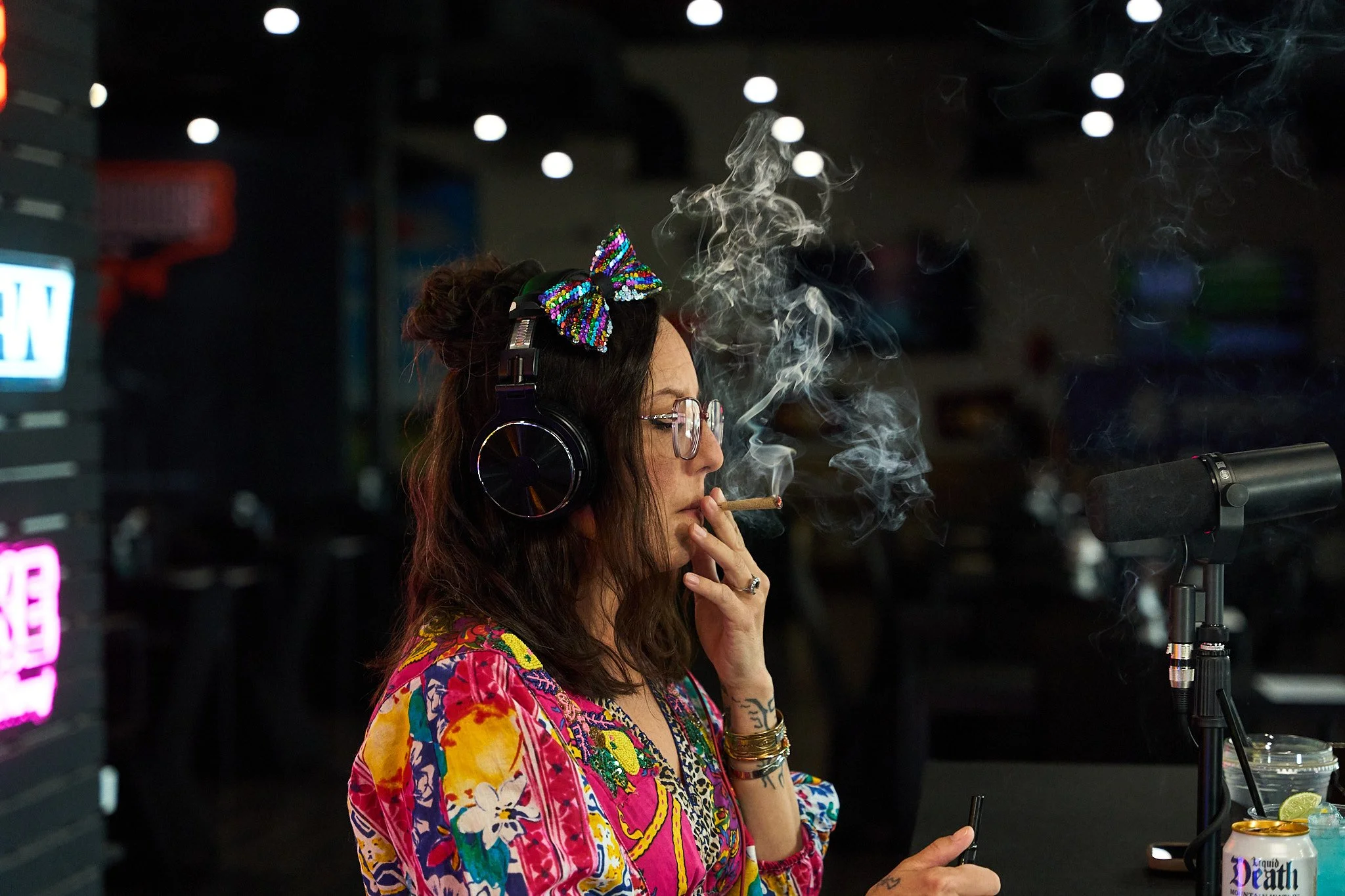 Jenn Tramaglino smoking a joint while speaking during the NuWu Sessions Podcast recording at Sky High Lounge, surrounded by neon cannabis brand signage inside NuWu Main Dispensary.