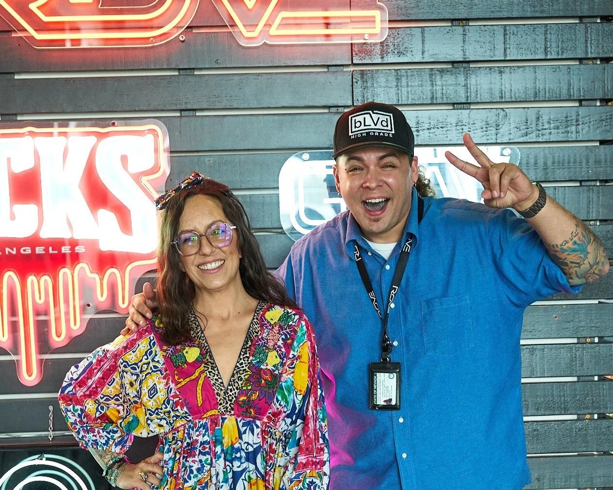 NuWu Sessions Podcast host Tom Nieves and guest Jenn Tramaglino posing in front of the neon cannabis brand wall inside Sky High Lounge at NuWu Main Dispensary in downtown Las Vegas.