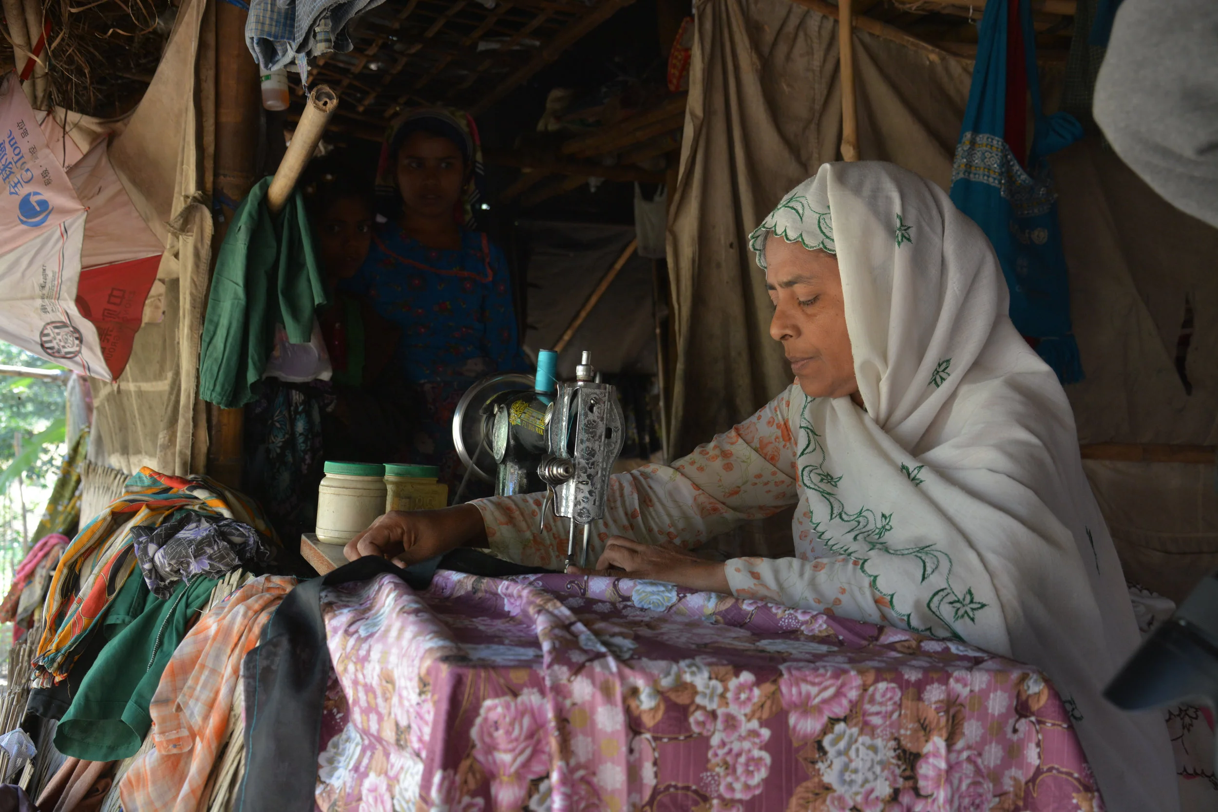 Daw Swe at her sewing machine, while her daughters look on.