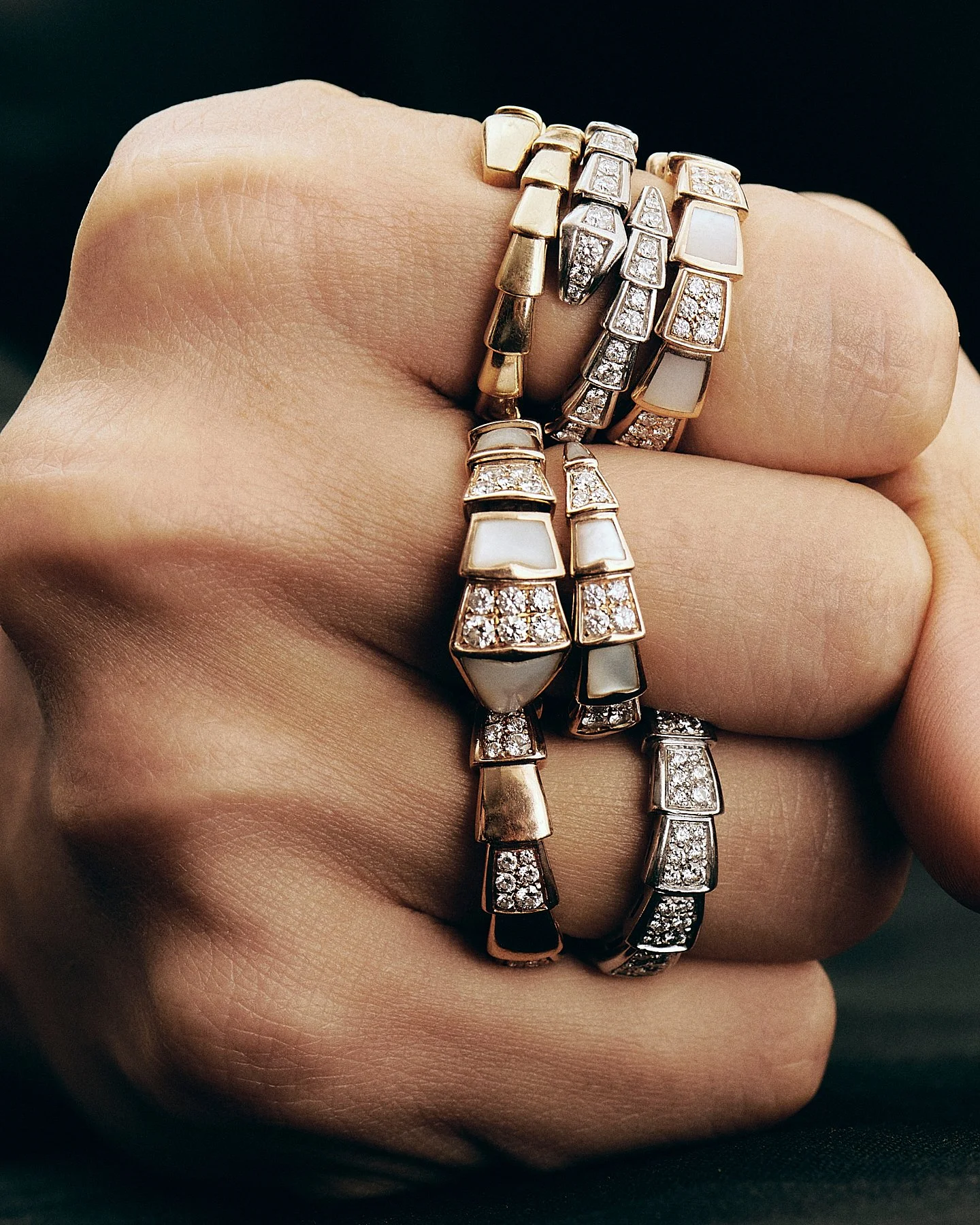 Multiple gold, silver, and rose gold rings with diamonds and white inlays worn on a hand.