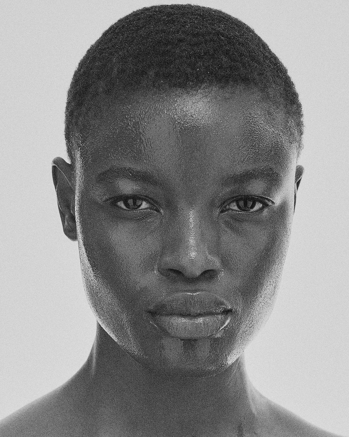 Close-up black and white portrait of a person with short hair, looking directly at the camera, with a neutral expression.
