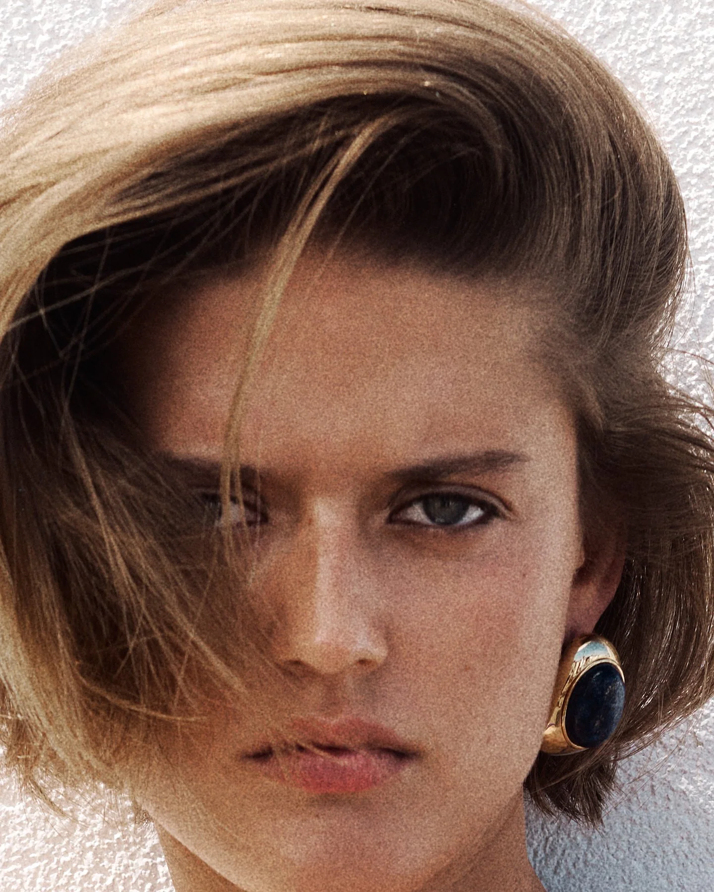 Close-up of a woman with light brown hair with blonde highlights, wearing large earrings, and with a neutral expression.