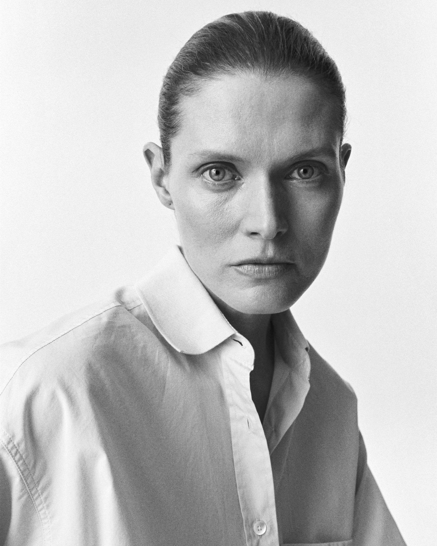 Black and white portrait of a woman with hair pulled back, wearing a collared shirt, looking directly at the camera against a plain background.