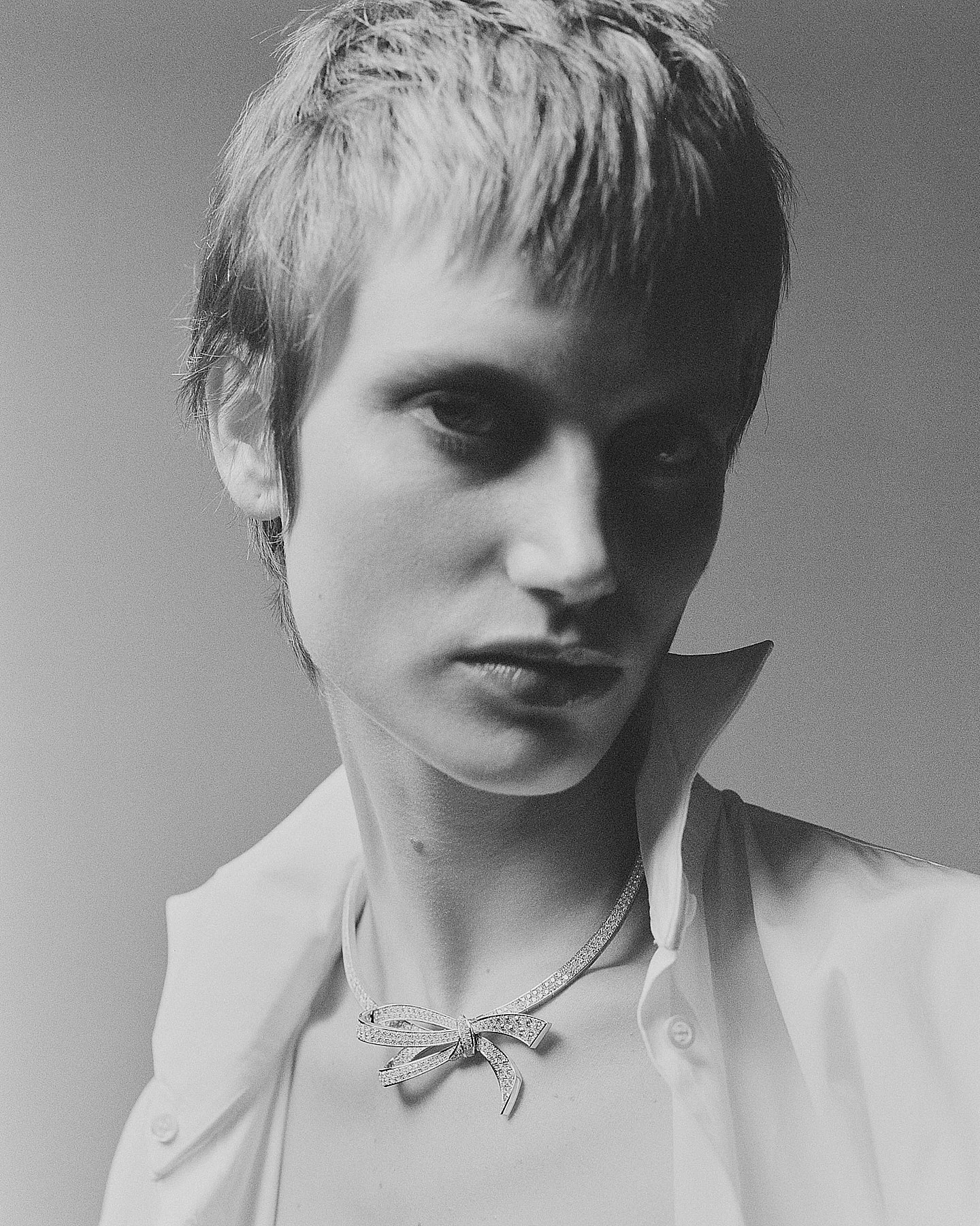 Black and white portrait of a woman with short hair, wearing a blouse and a decorative bow necklace.