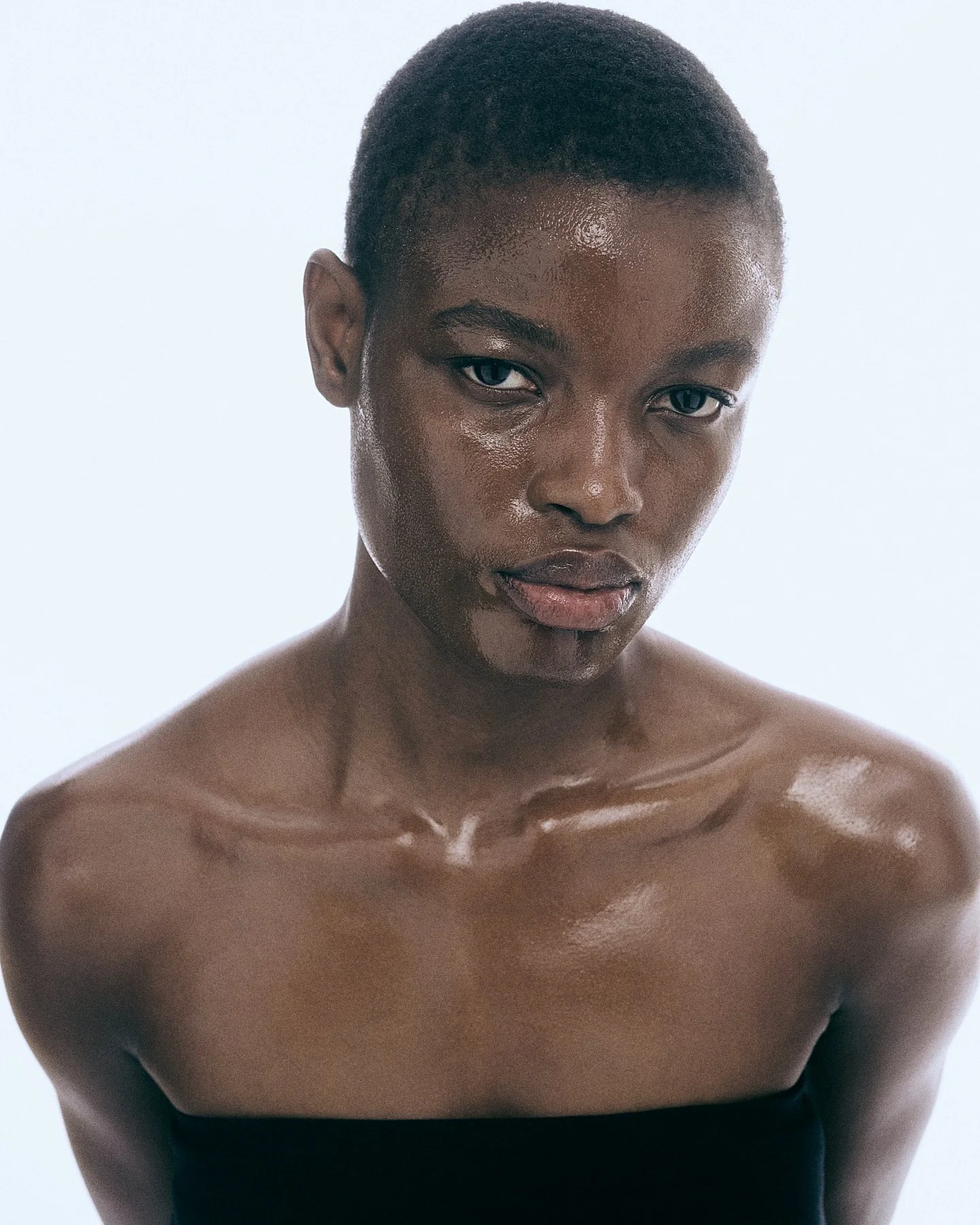 A topless woman with dark skin, short hair, and dark eyes looking directly at the camera against a white background.
