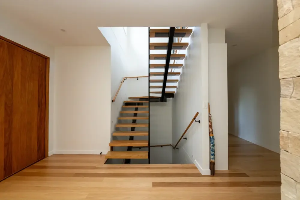Modern timber staircase with open risers and black steel stringers, set against white walls and hardwood flooring.