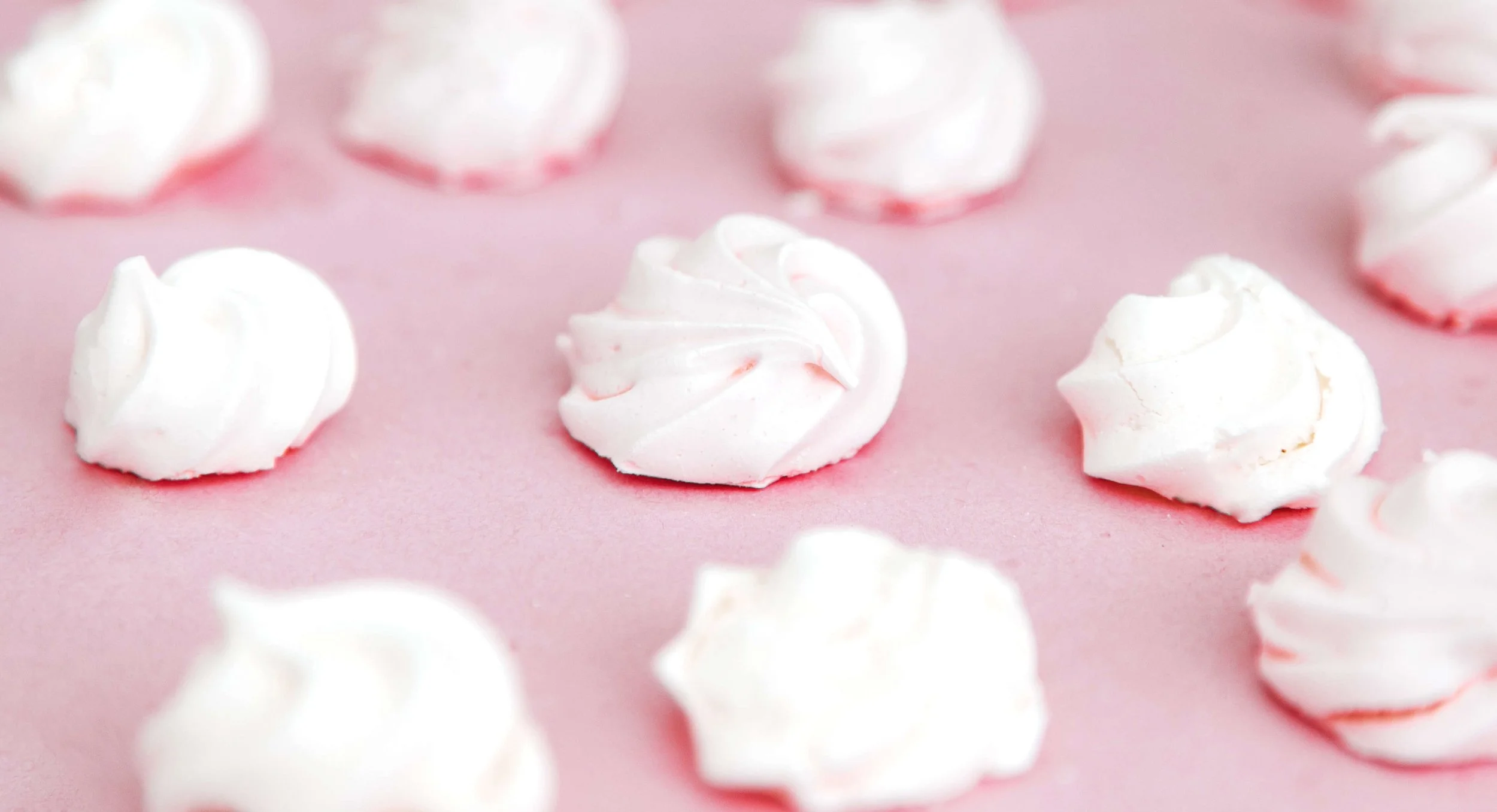 White meringues on a light pink background.