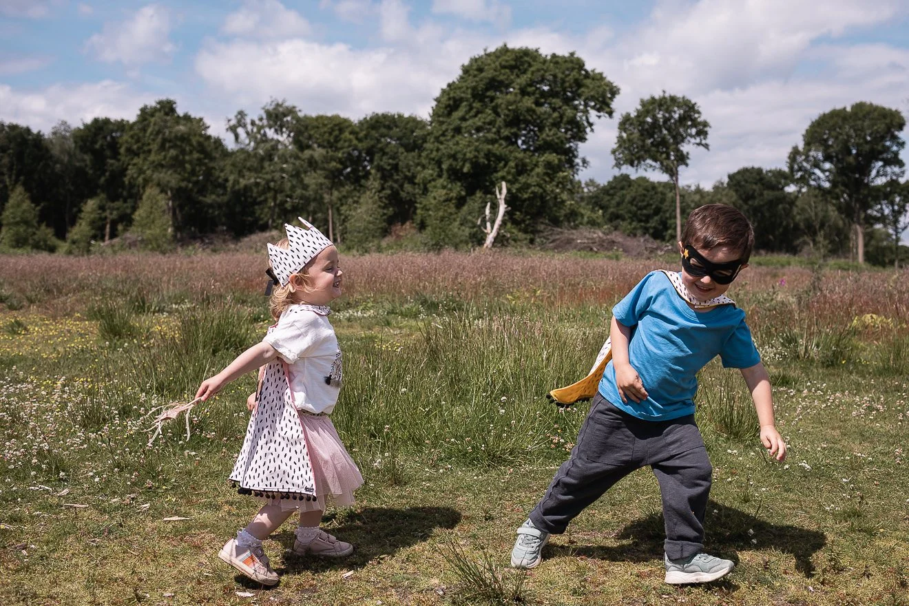 Young superheroes wearing handmade capes, crown and masks chasing each other.
