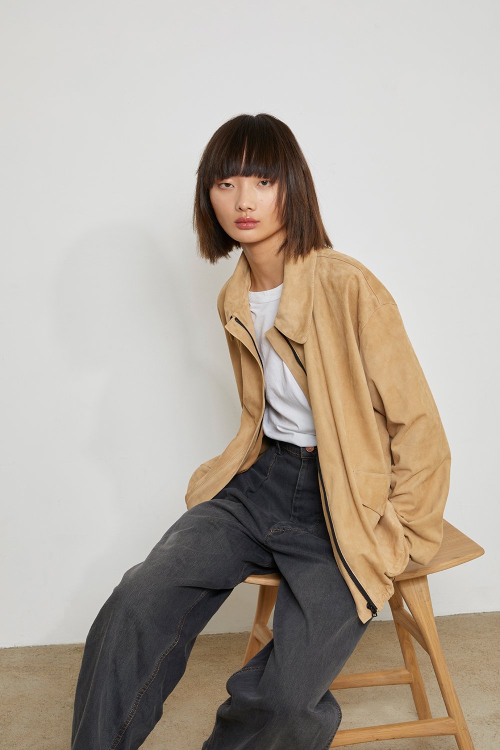 Studio fashion editorial with beige suede masculin jacket, grey trousers and seated model composition.