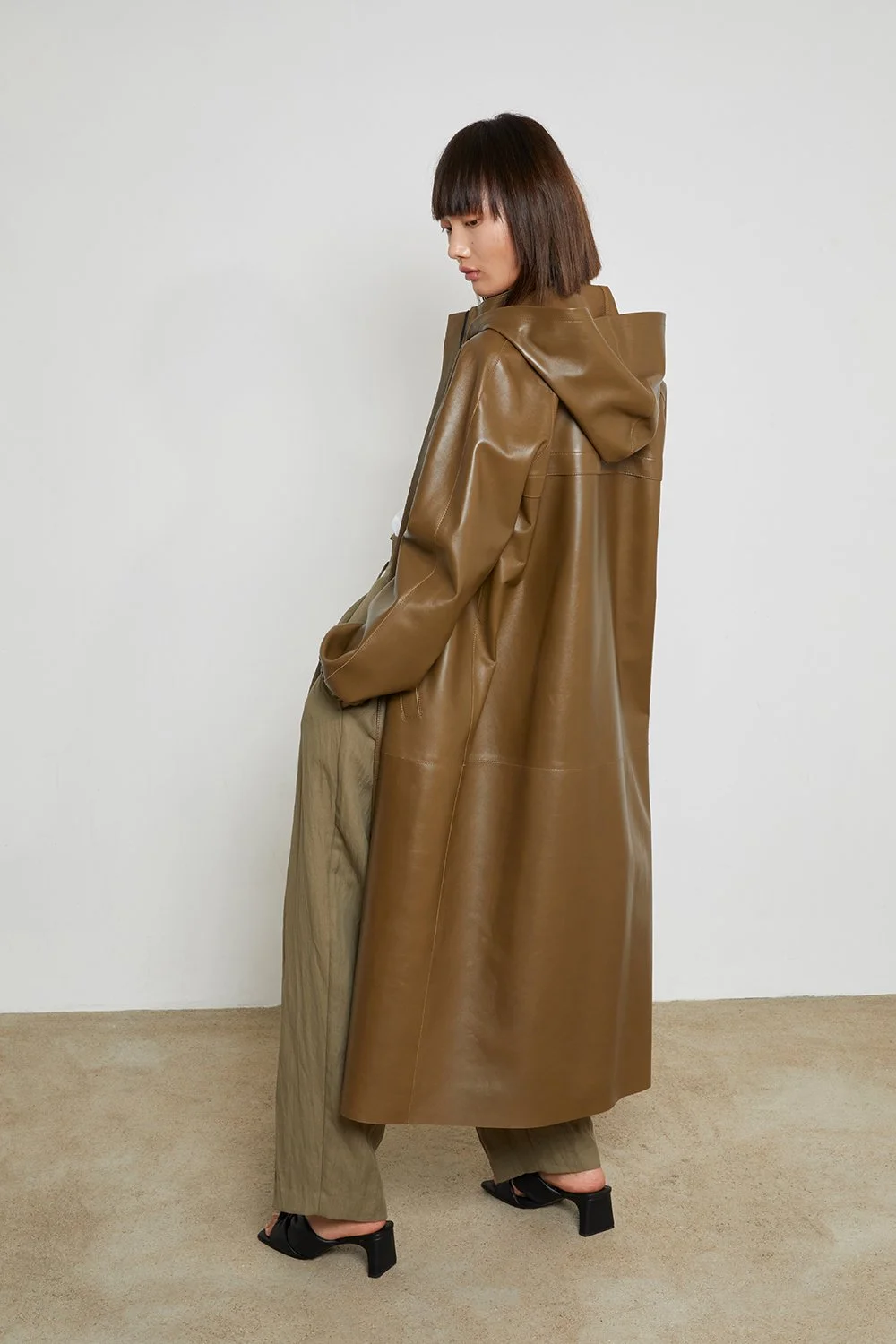 Luxury outerwear editorial with brown leather coat, hood detail and minimal studio composition.