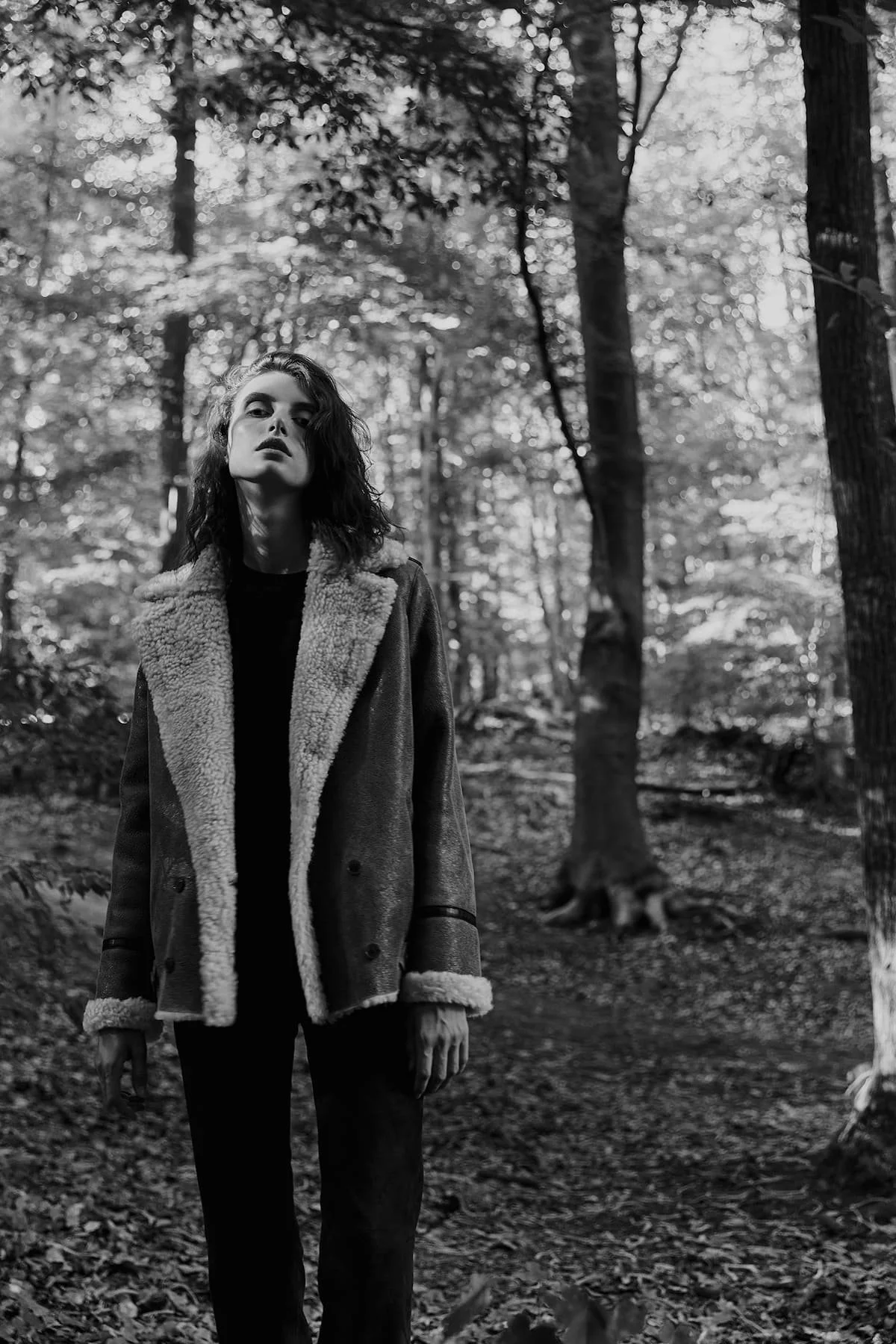 Black and white fashion editorial portrait in forest setting with shearling jacket.