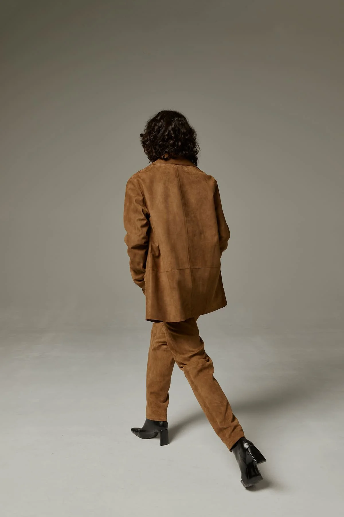 Fashion editorial look with brown suede suit, back-view pose and modern studio direction.