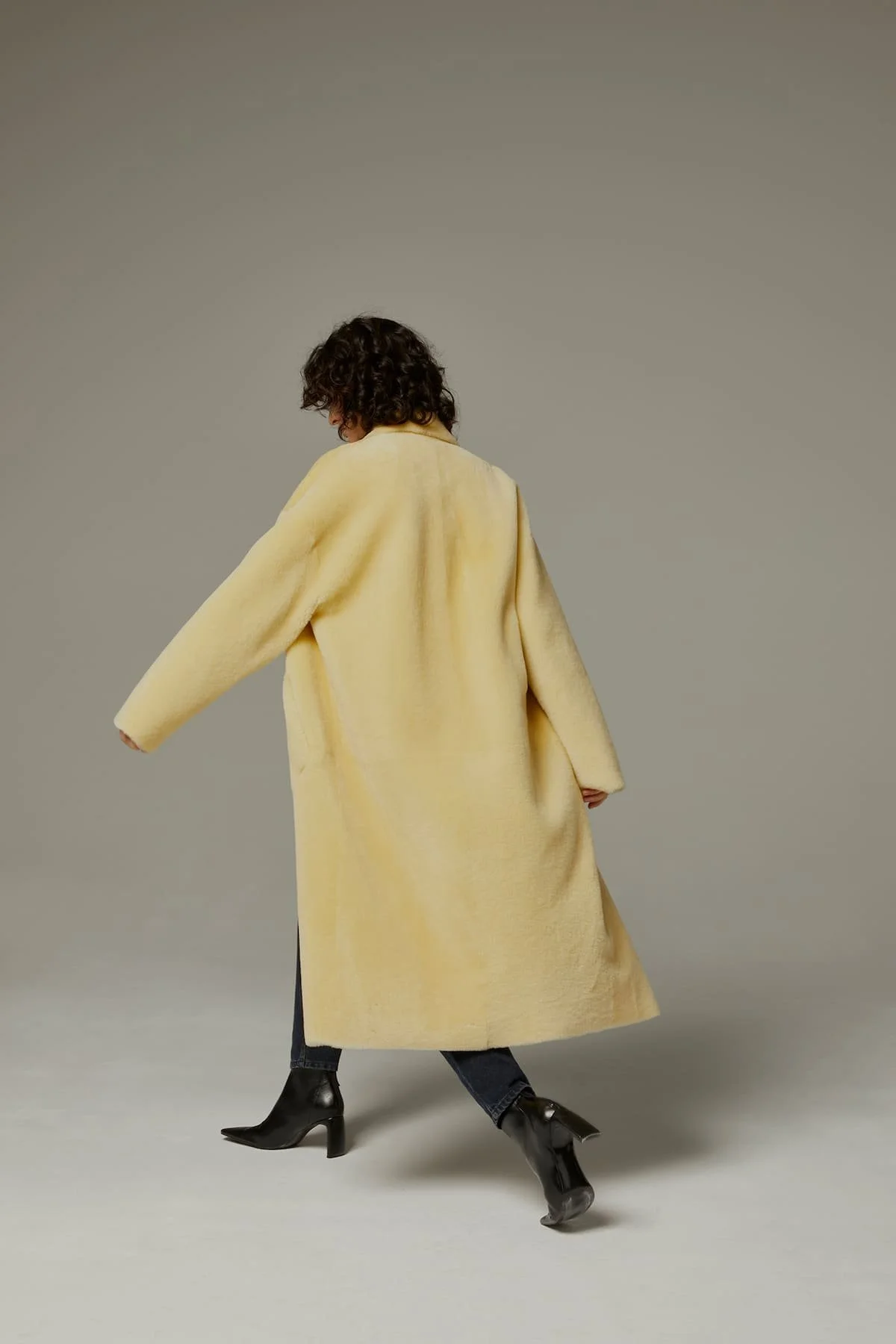 Editorial fashion image with pale yellow coat, movement and modern outerwear styling.