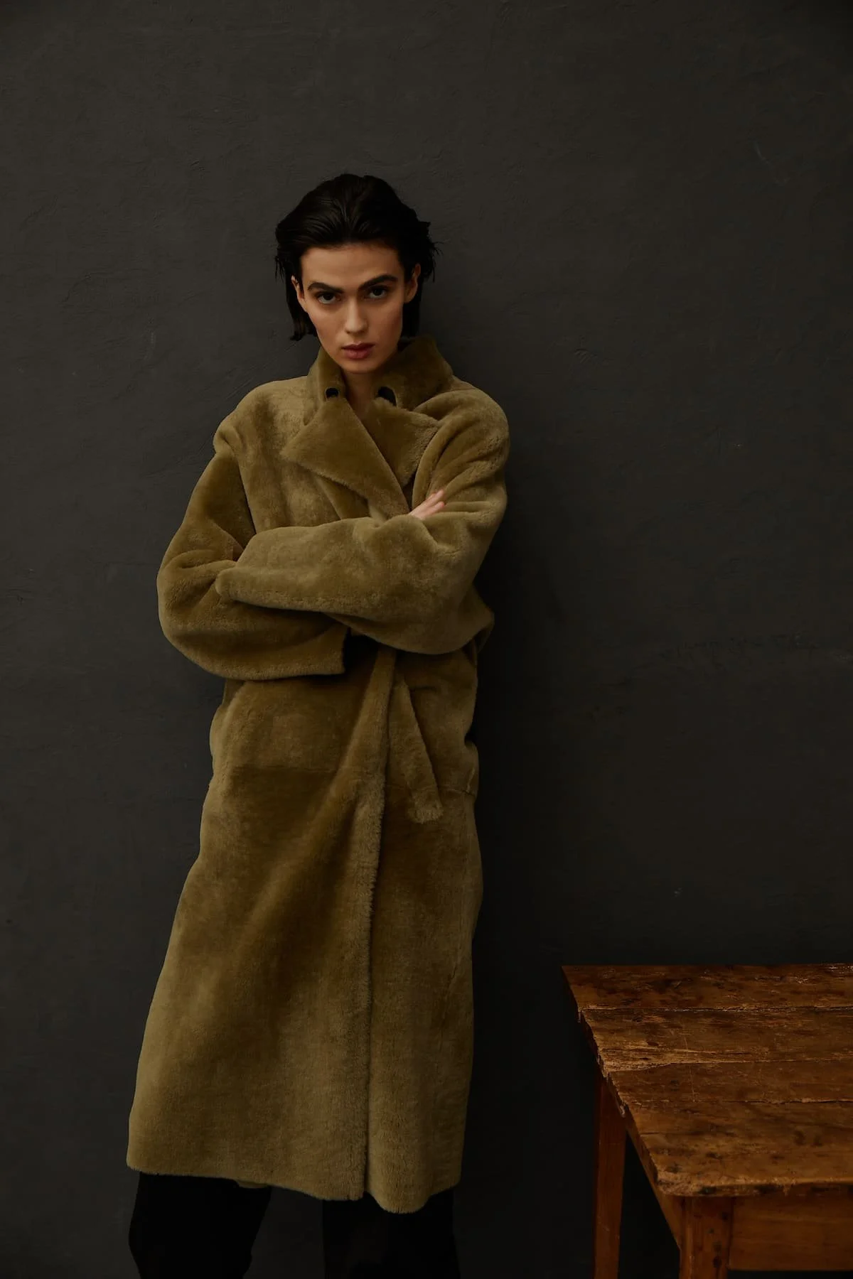 Fashion editorial portrait with olive shearling coat, dark background and refined visual direction.