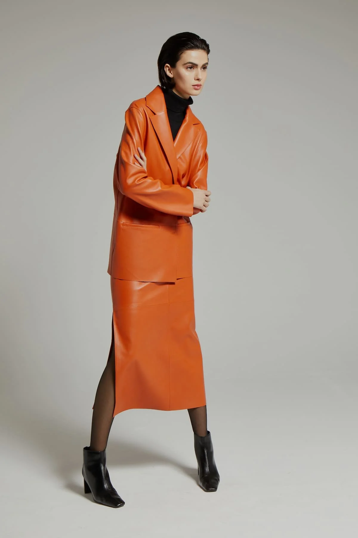 Luxury fashion editorial with orange leather jacket and leather skirt and strong studio composition.