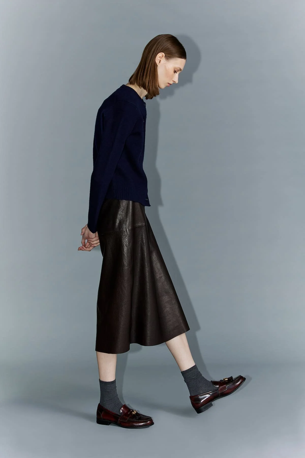 Minimal fashion editorial with navy knitwear, leather skirt and clean studio direction.