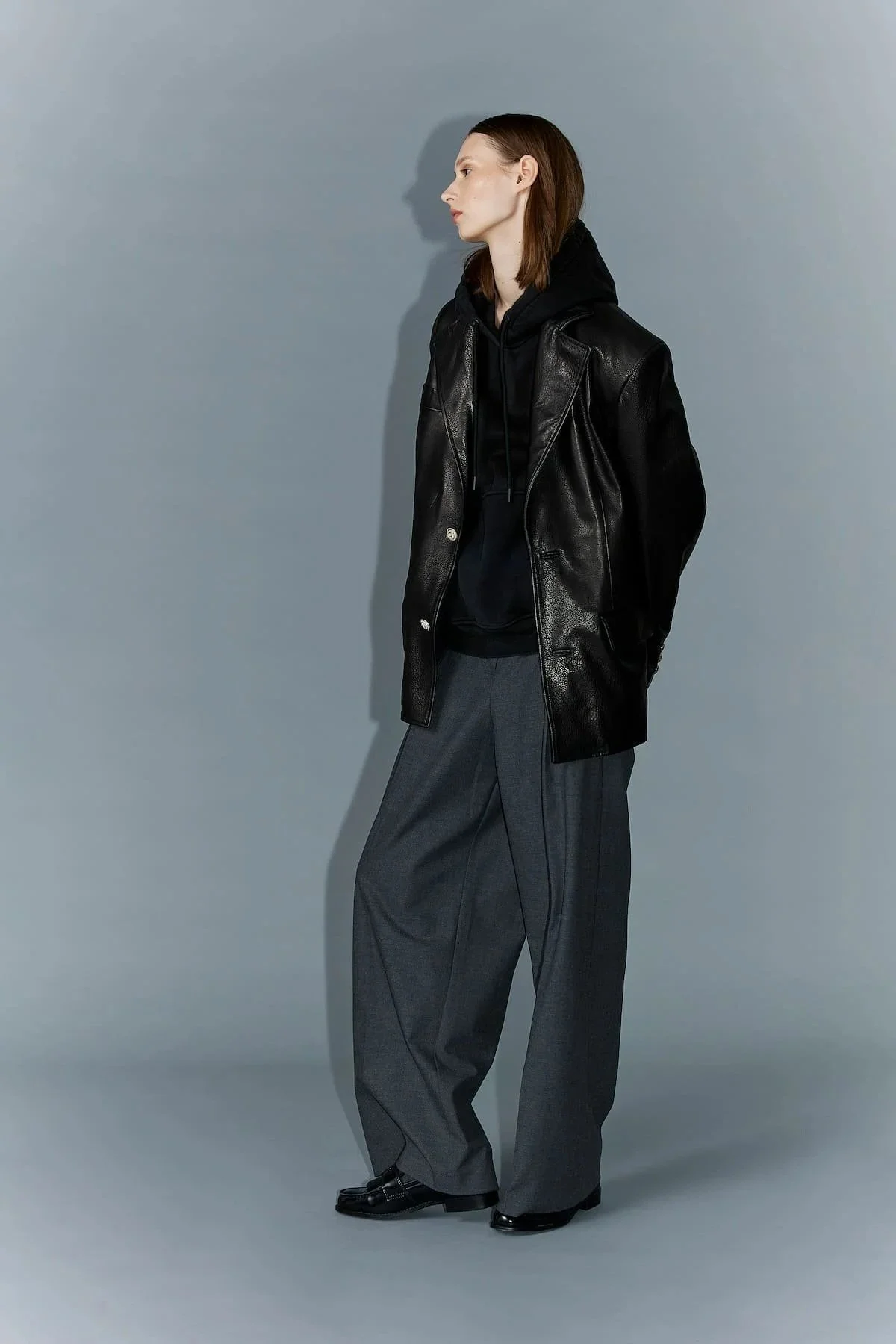 Fashion editorial look with black leather jacket, wide trousers and cool studio pose.