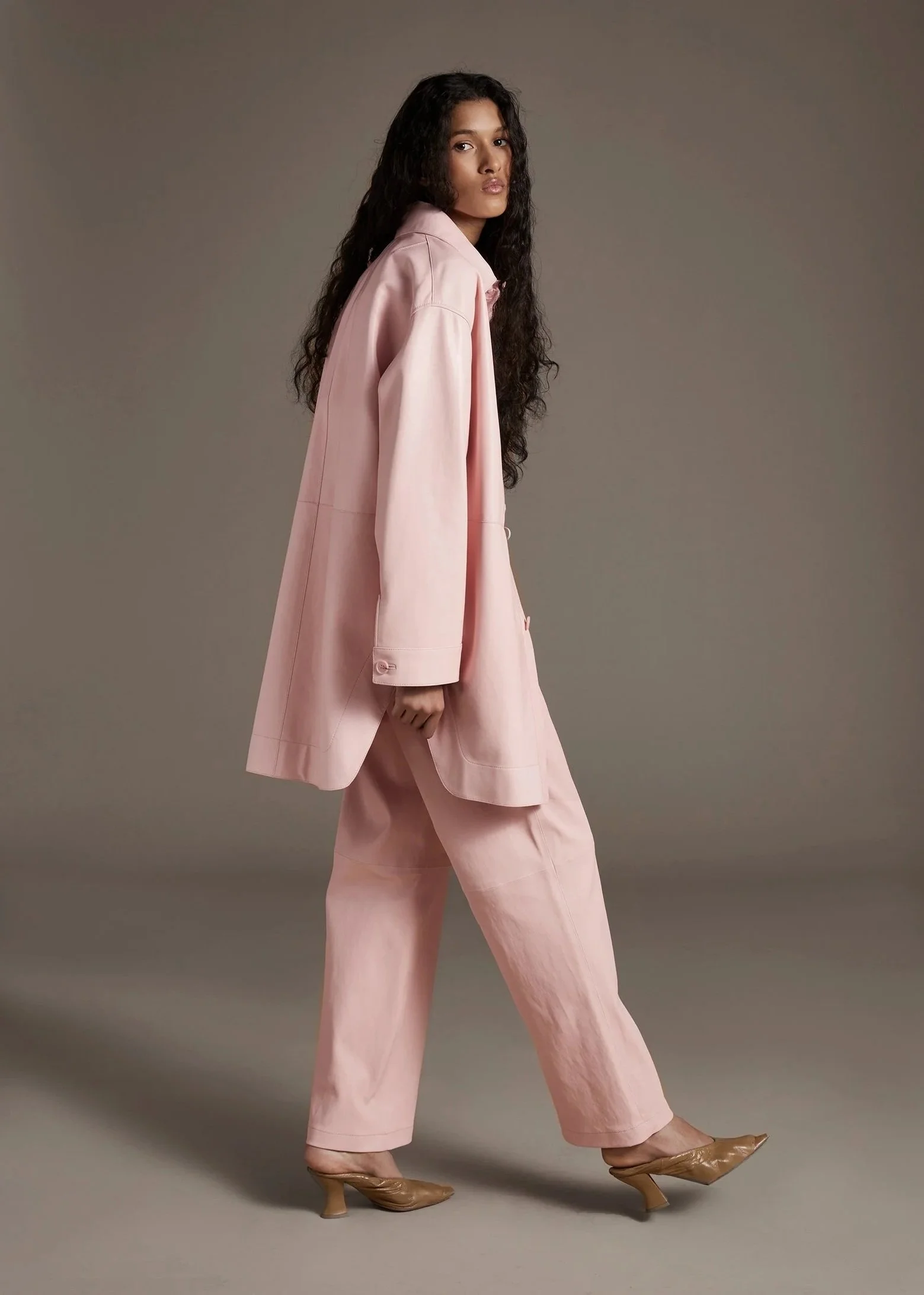 Fashion editorial look with pale pink leather sustainable suit, soft tailoring and studio setting.